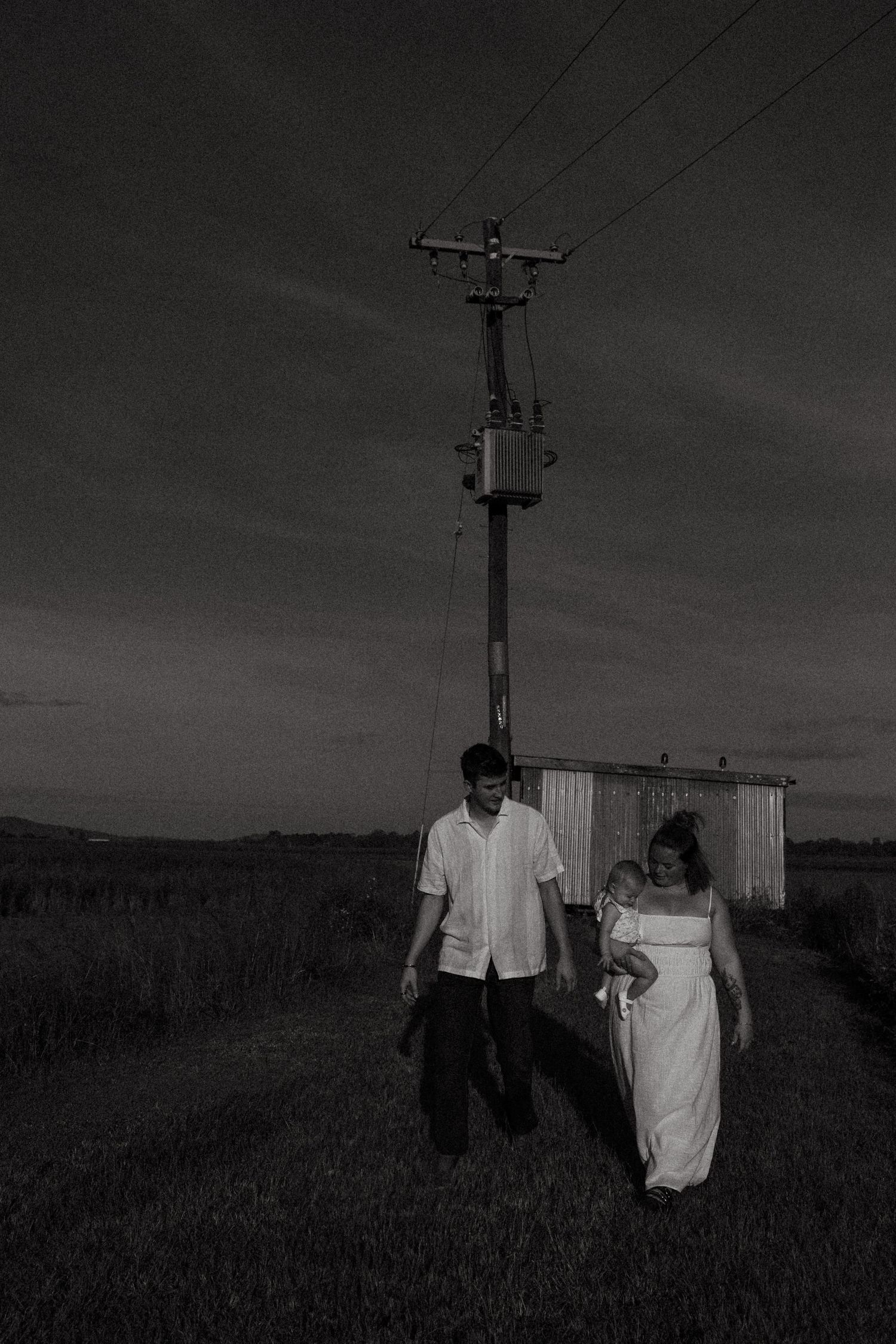 Black and white wedding photo of couple walking near utility pole at dusk.
