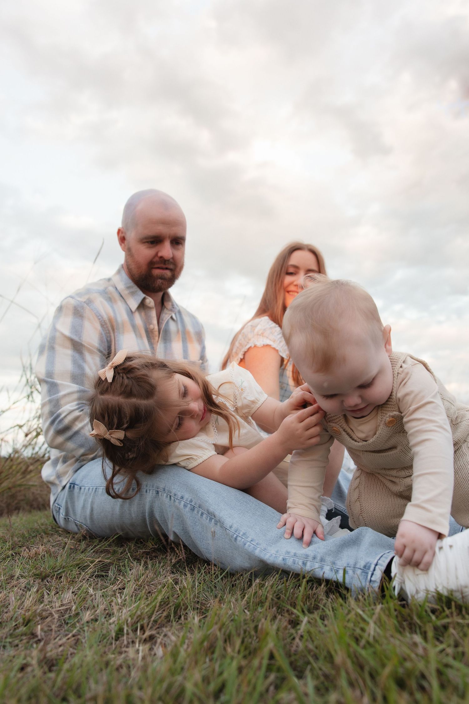 An intimate family portrait sequence shows tender moments between parents and baby laying together in grass at sunset.