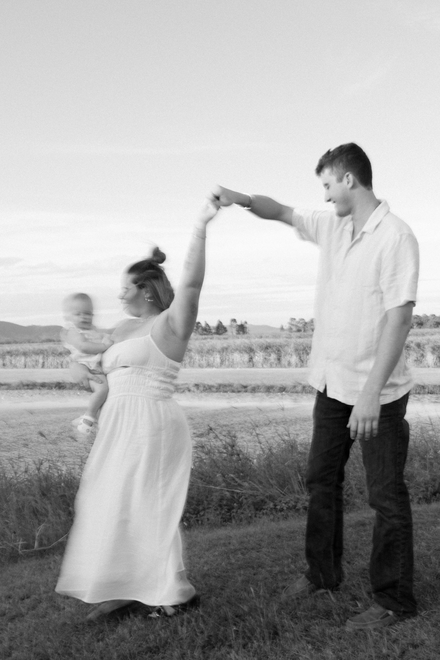 A couple dancing together in a field at sunset with mountains in the background.