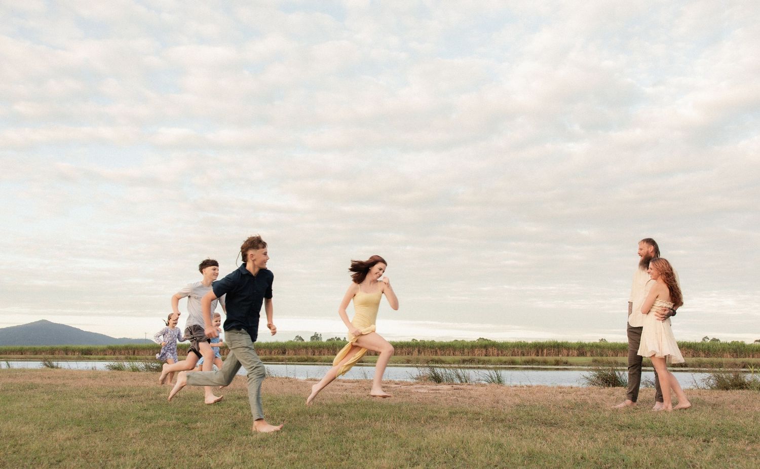 A group of friends running and playing together in a grassy field at sunset with mountains in the background.