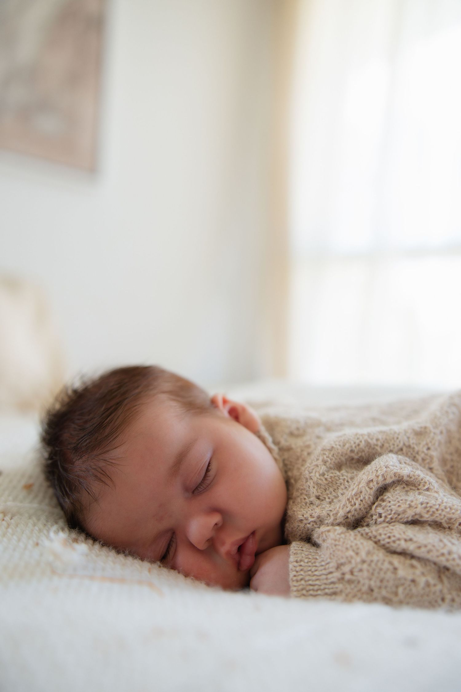 Peaceful close-up of sleeping infant in knit sweater on white bedding.