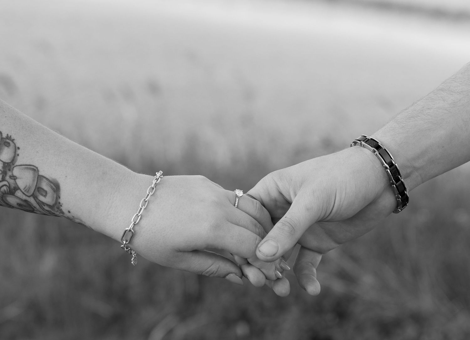 Close-up black and white shot of two hands with bracelets reaching towards each other tenderly against blurred background.