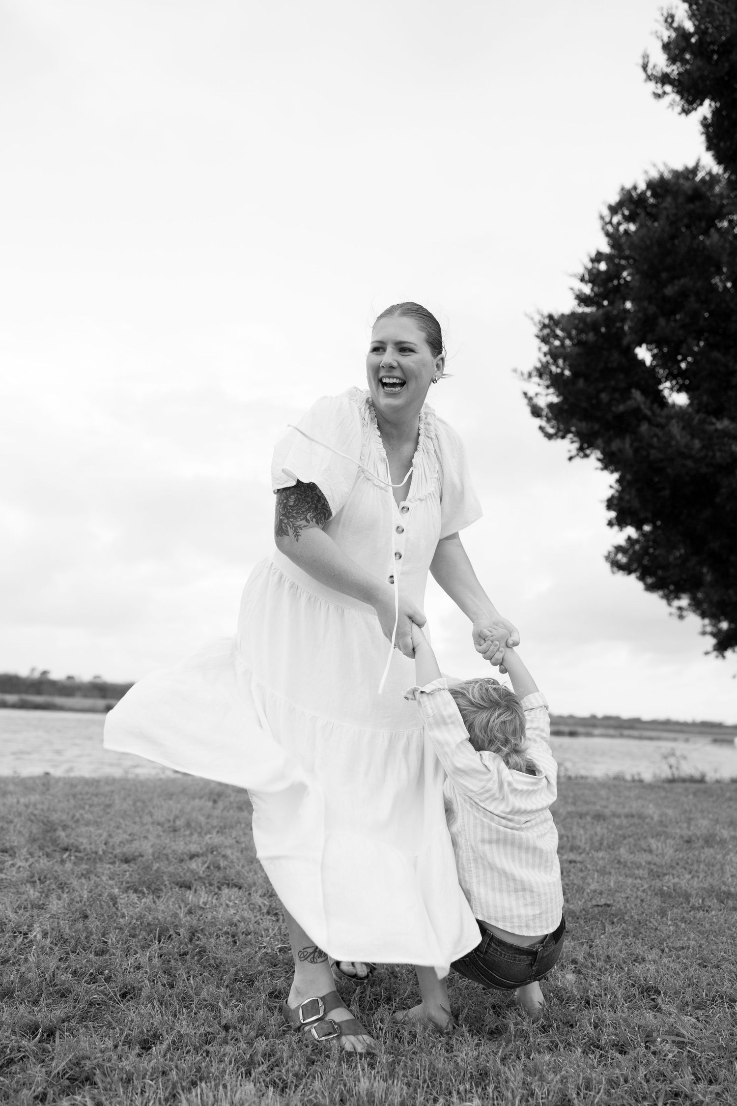 Someone in a flowing white dress spins playfully in a field near water.