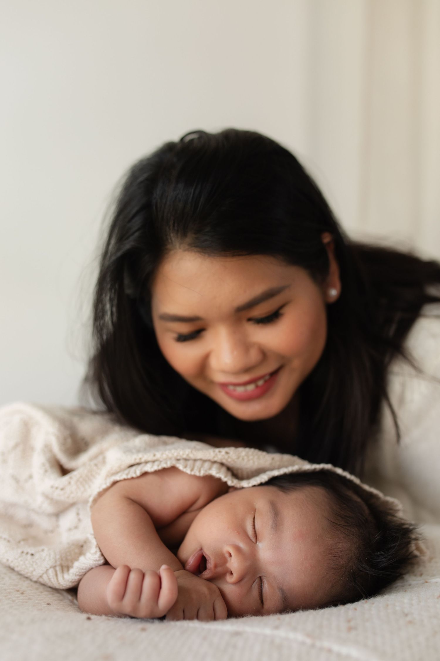 A tender moment between a parent and sleeping newborn baby on soft white bedding.