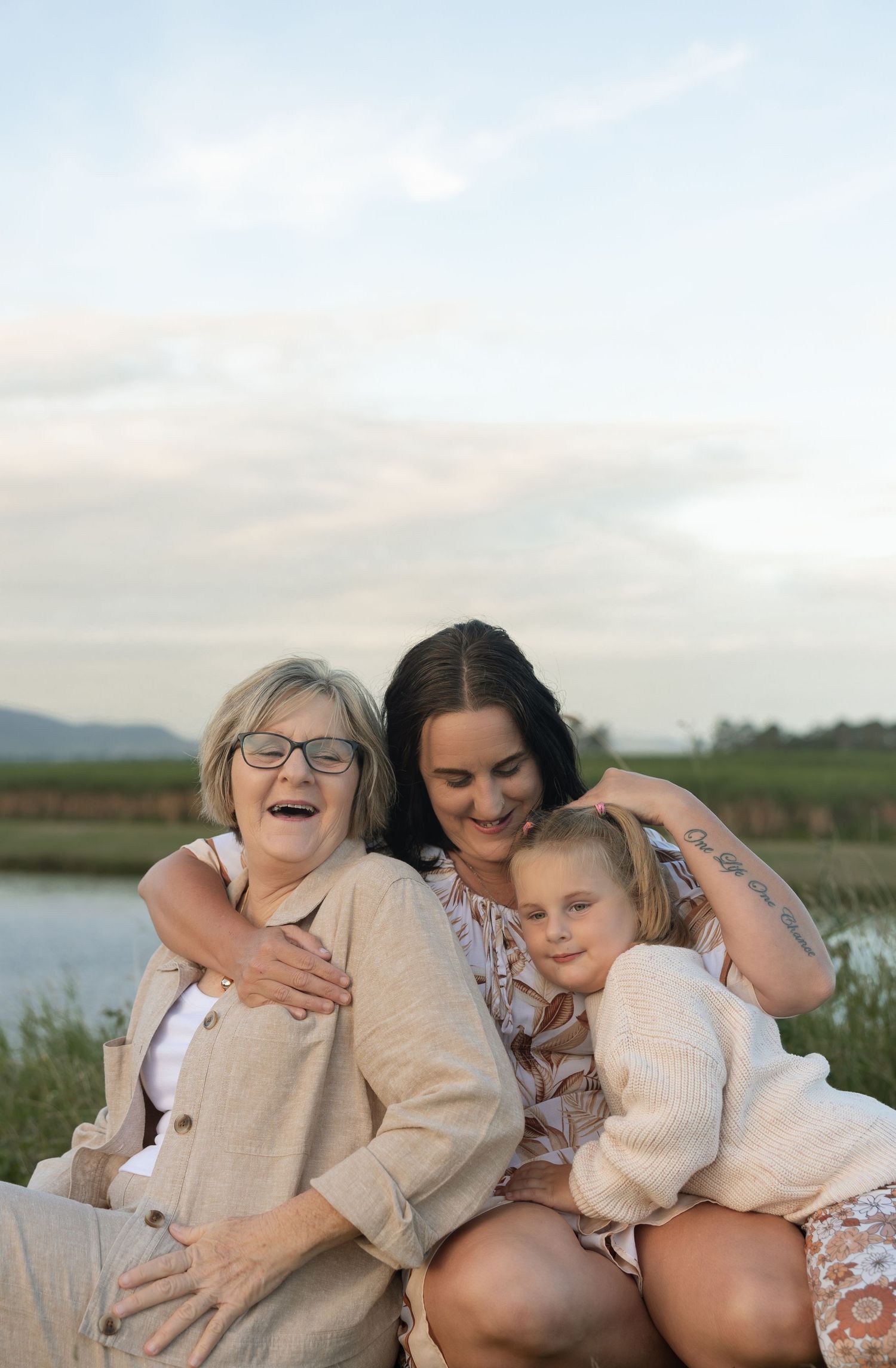 Joyful family embrace captured against serene lakeside landscape at sunset.