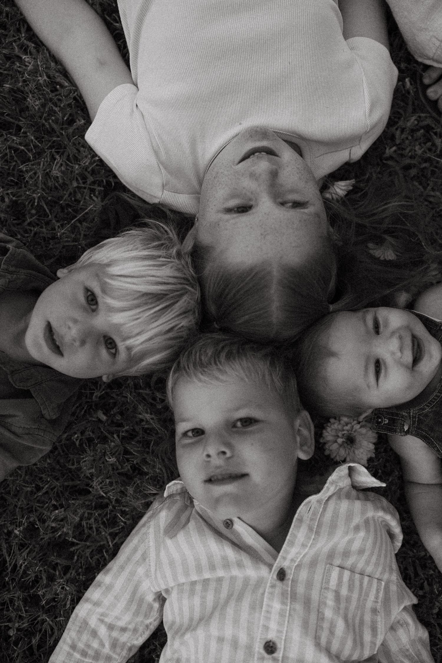 Black and white overhead portrait of children laying in a circle on grass.