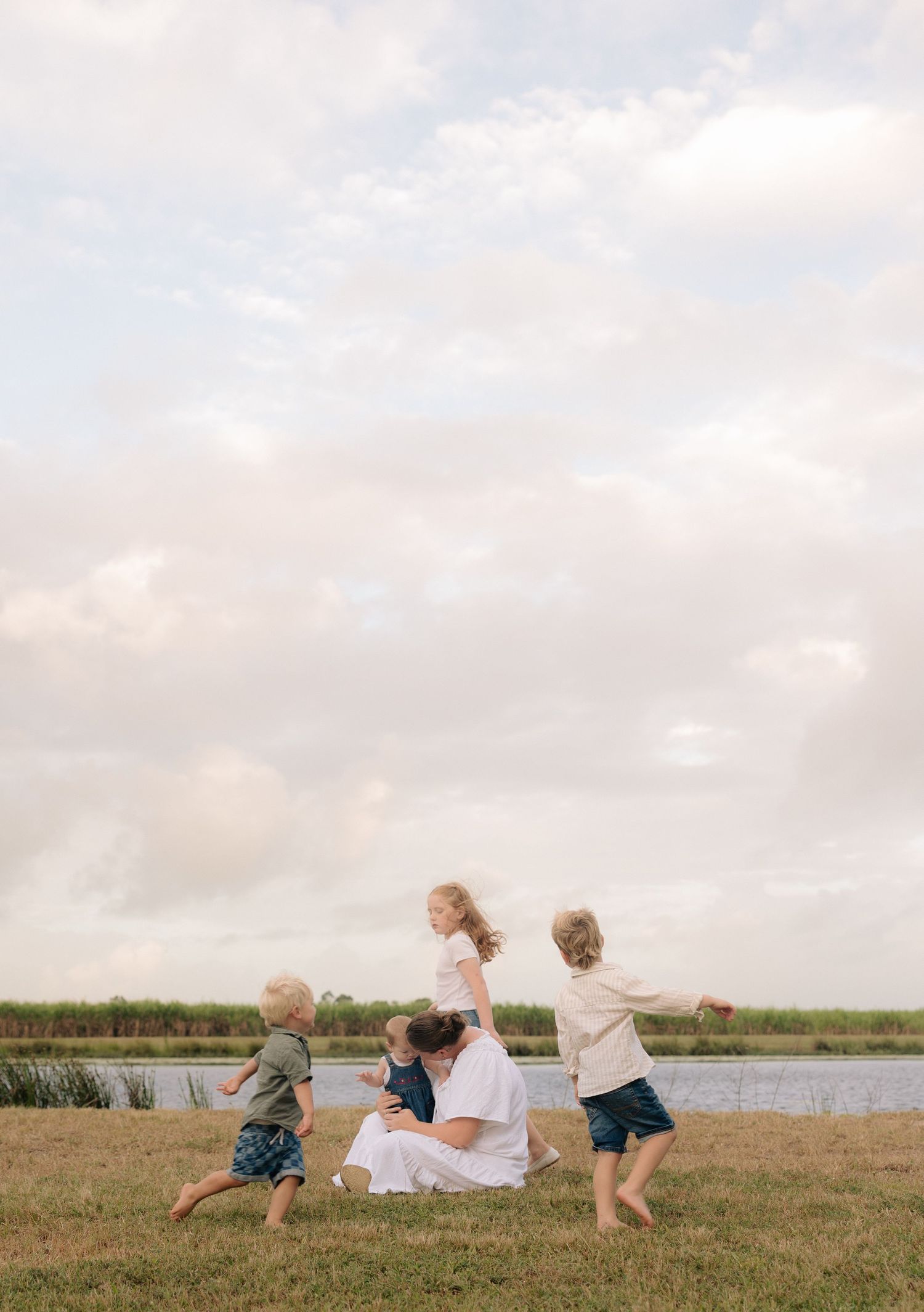 Group playing together on grassy field beside waterway under cloudy sky.