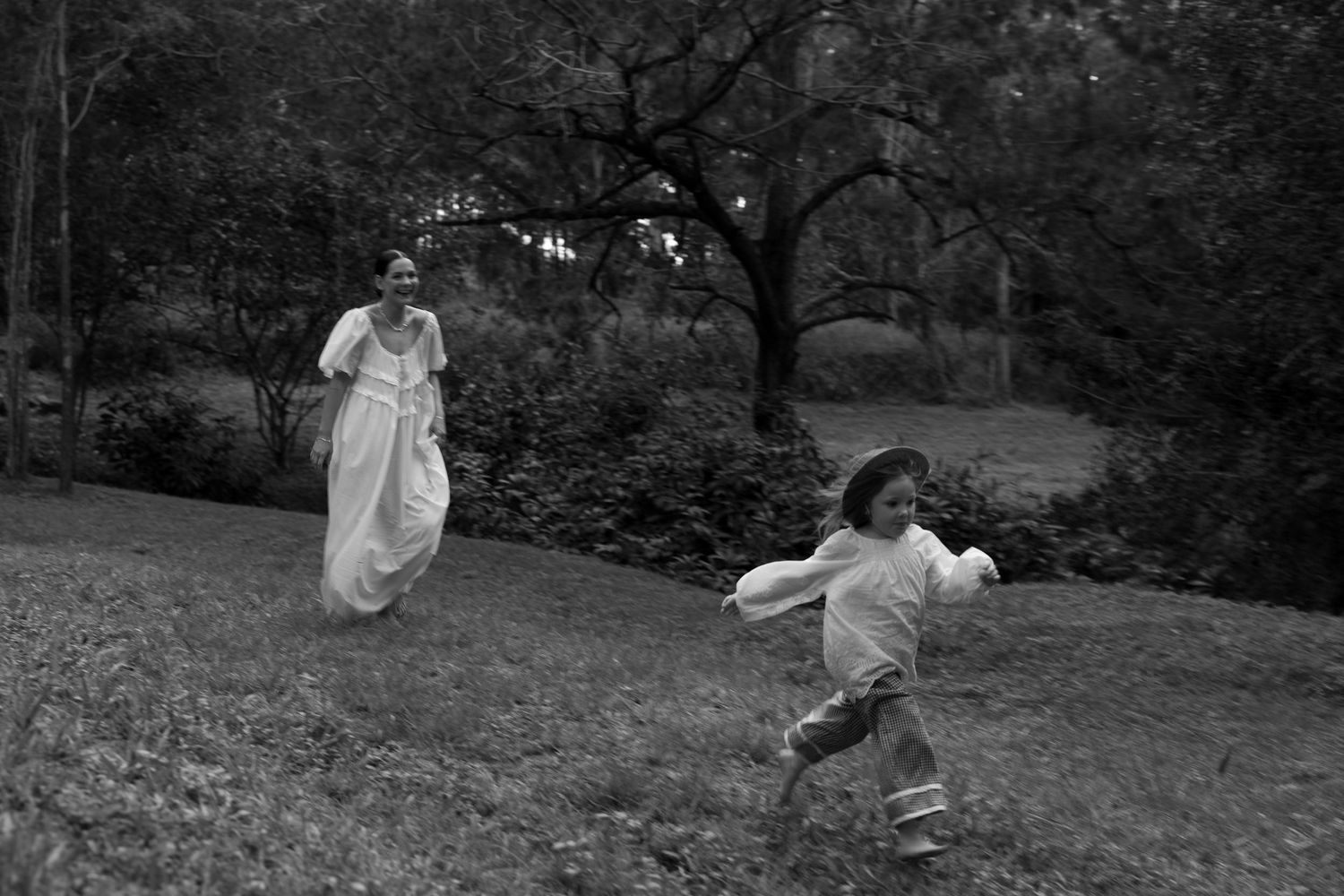 Two people in white dresses dance joyfully across a grassy hillside in this vintage black and white photograph.