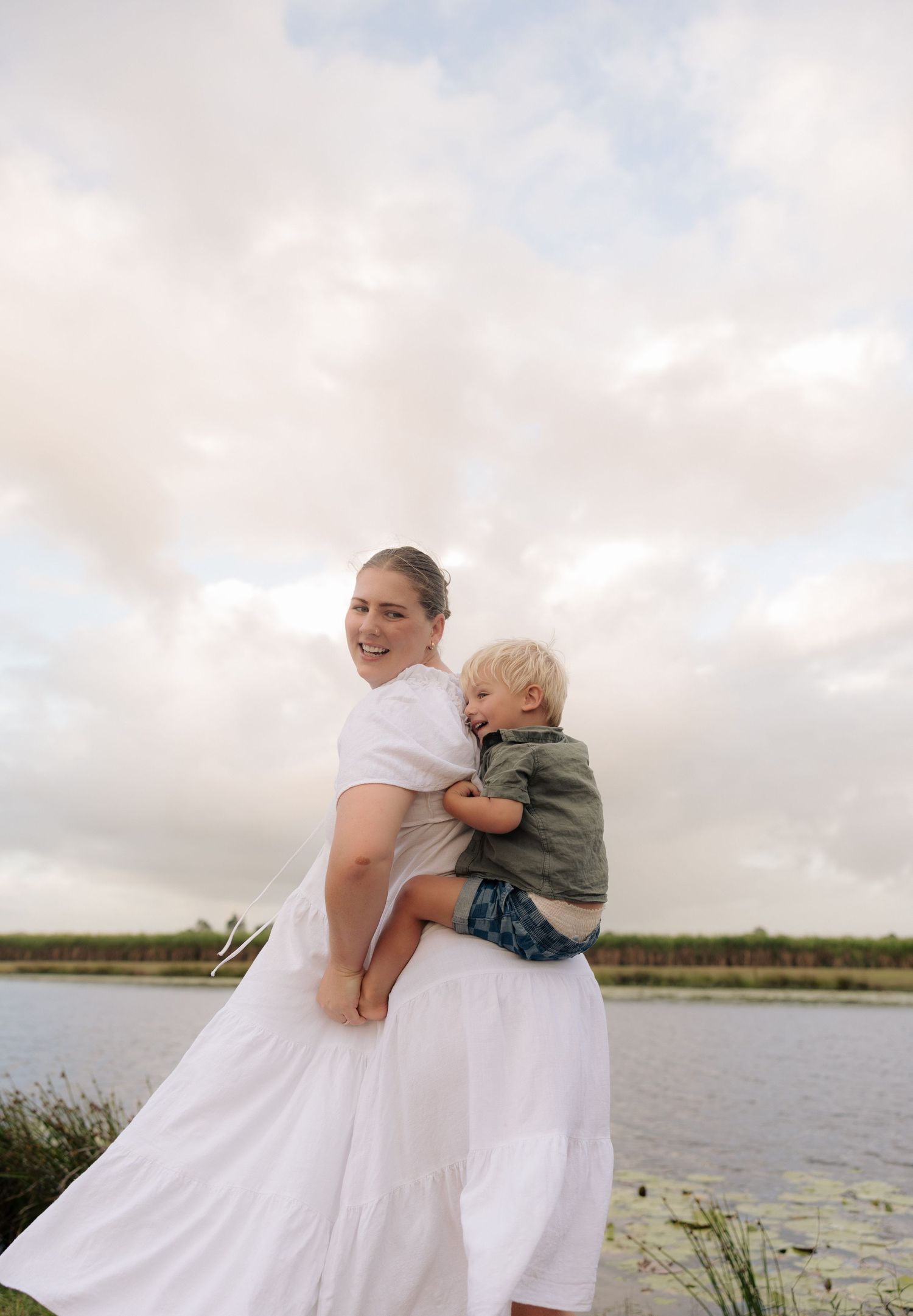 Parent and child sharing a warm hug by a peaceful lake under cloudy skies.