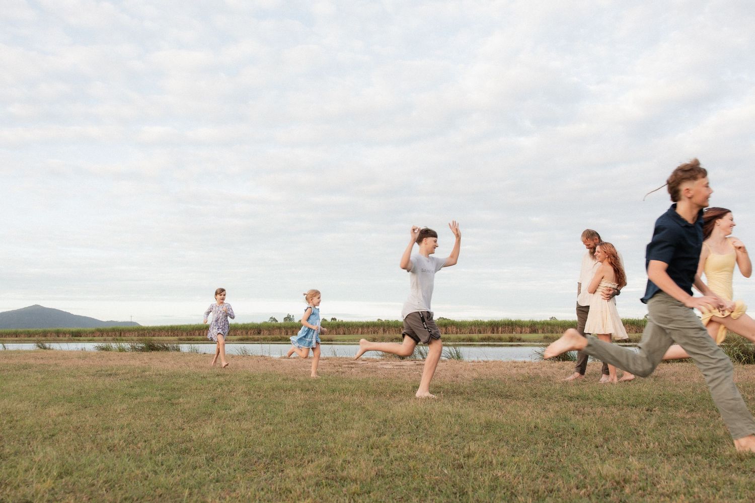 A group of people joyfully jumping in sync on a grassy field with mountains in the background on a cloudy day.