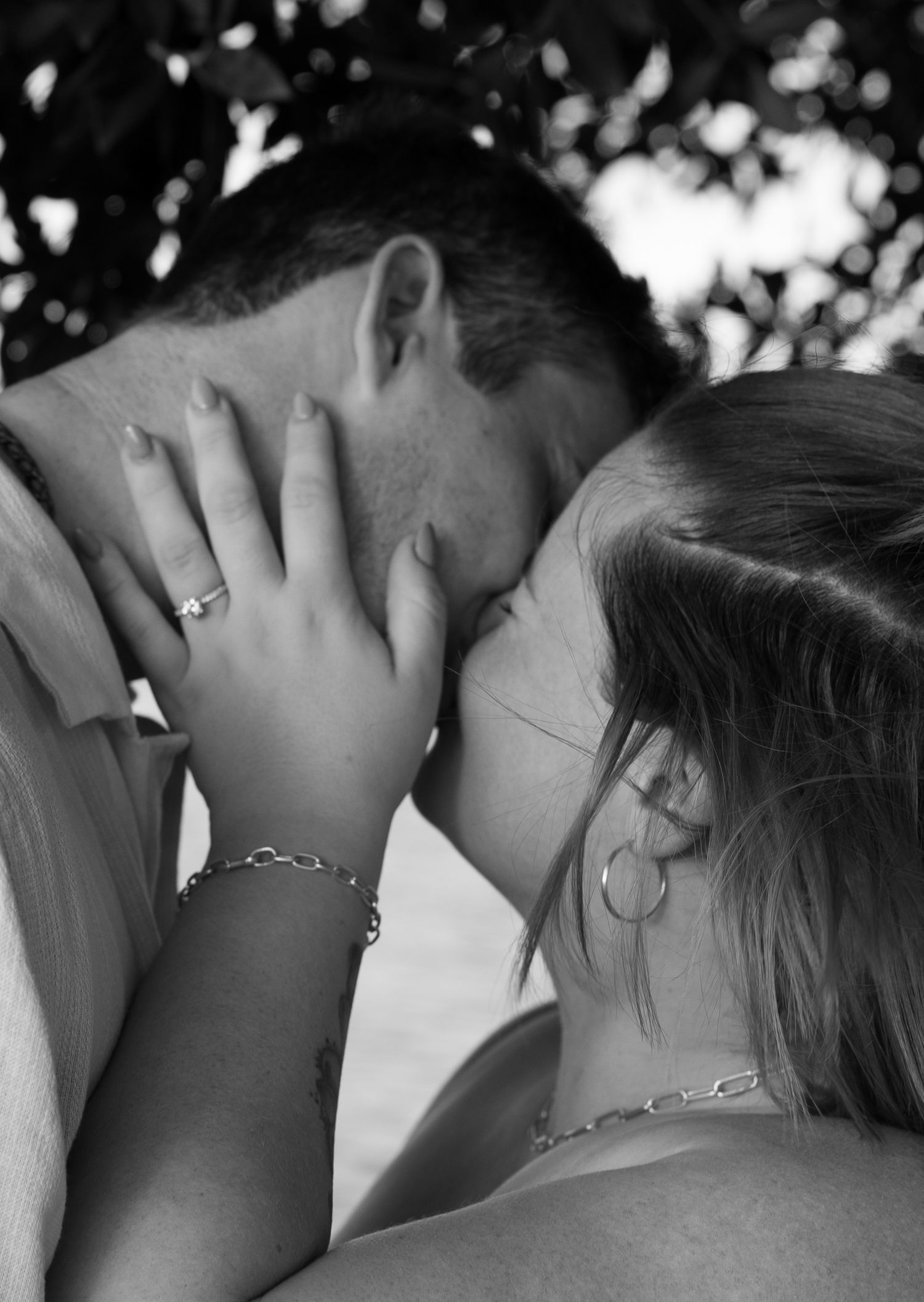 A romantic black and white photograph captures an intimate moment between a couple in soft natural lighting.