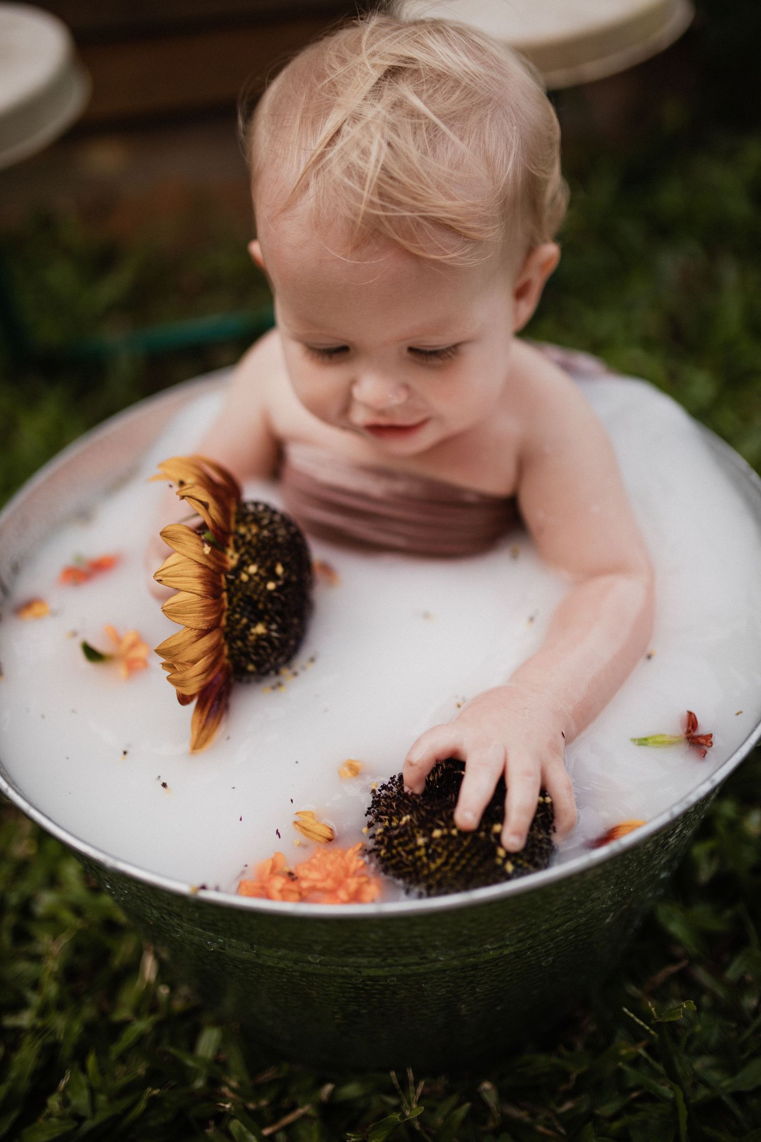 Creative photoshoot with sunflower and metal tub on grassy background.