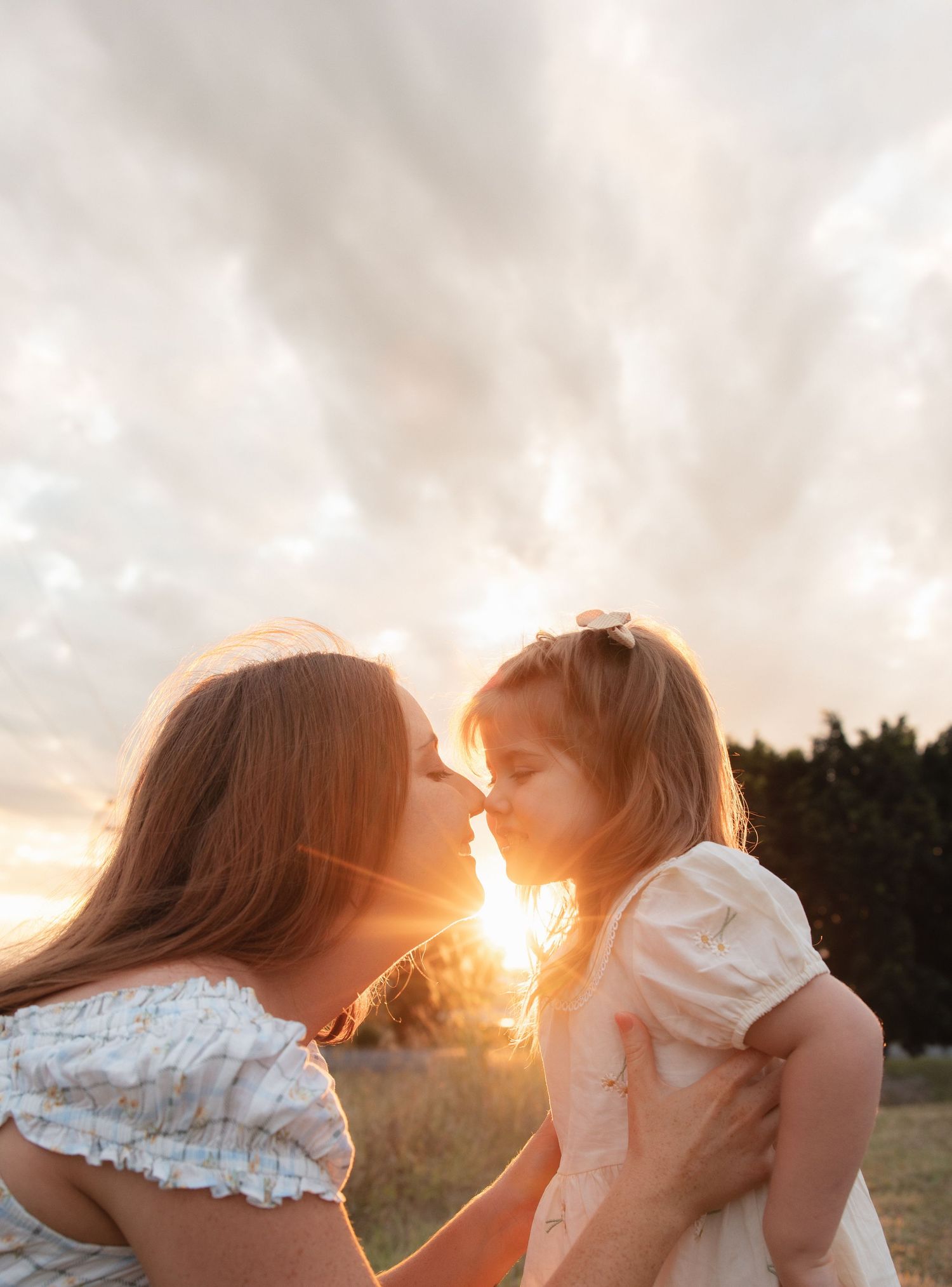 A tender moment between a woman and child silhouetted against a golden sunset in a grassy field.