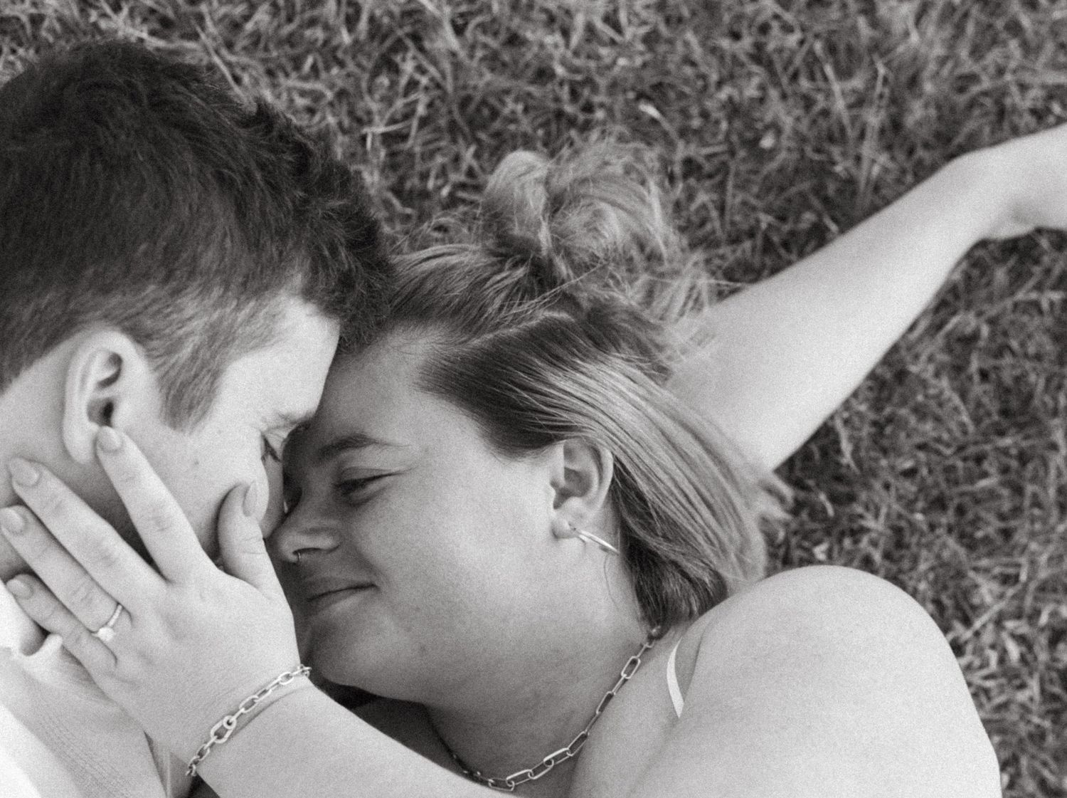 A romantic black and white photo of a couple lying close together in the grass.