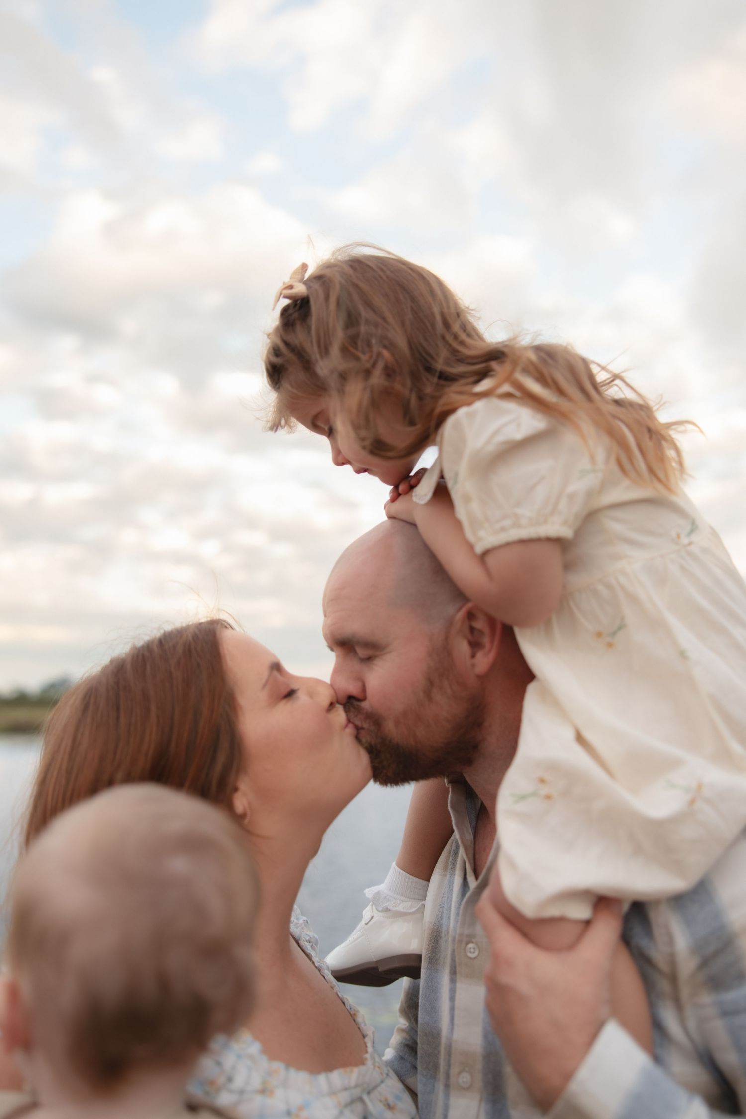 A loving family embraces in a tender moment outdoors against a cloudy sky background.