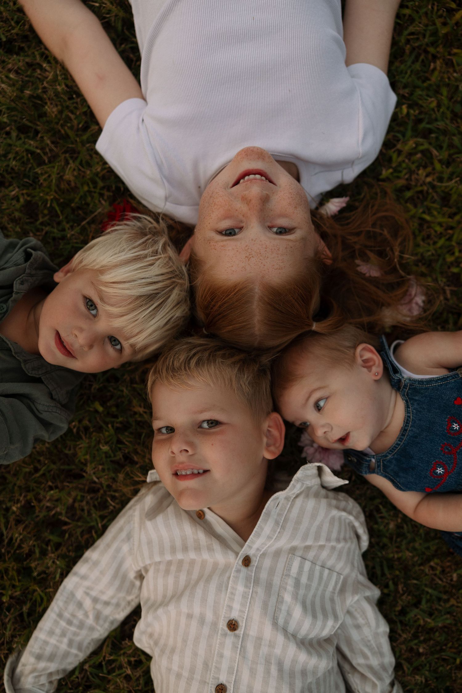 Group of children lying on grass in a circular formation looking up at the camera.