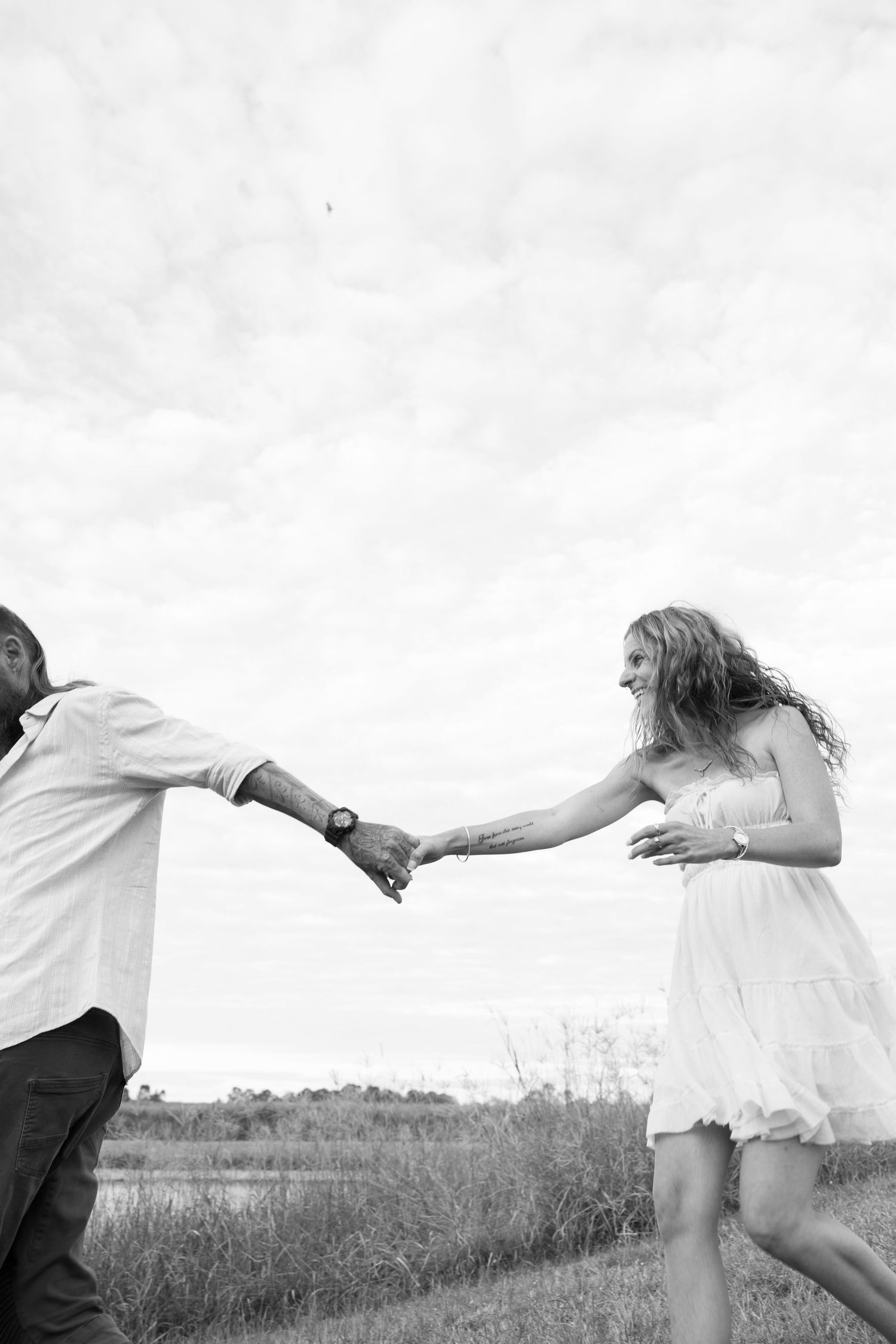 A romantic black and white photo shows a couple holding hands and running together in a grassy field.