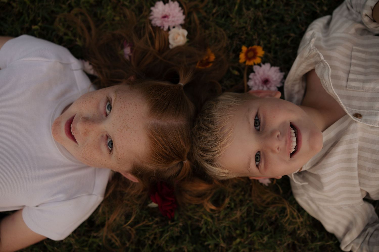 Two children lying on grass sharing a happy moment together.