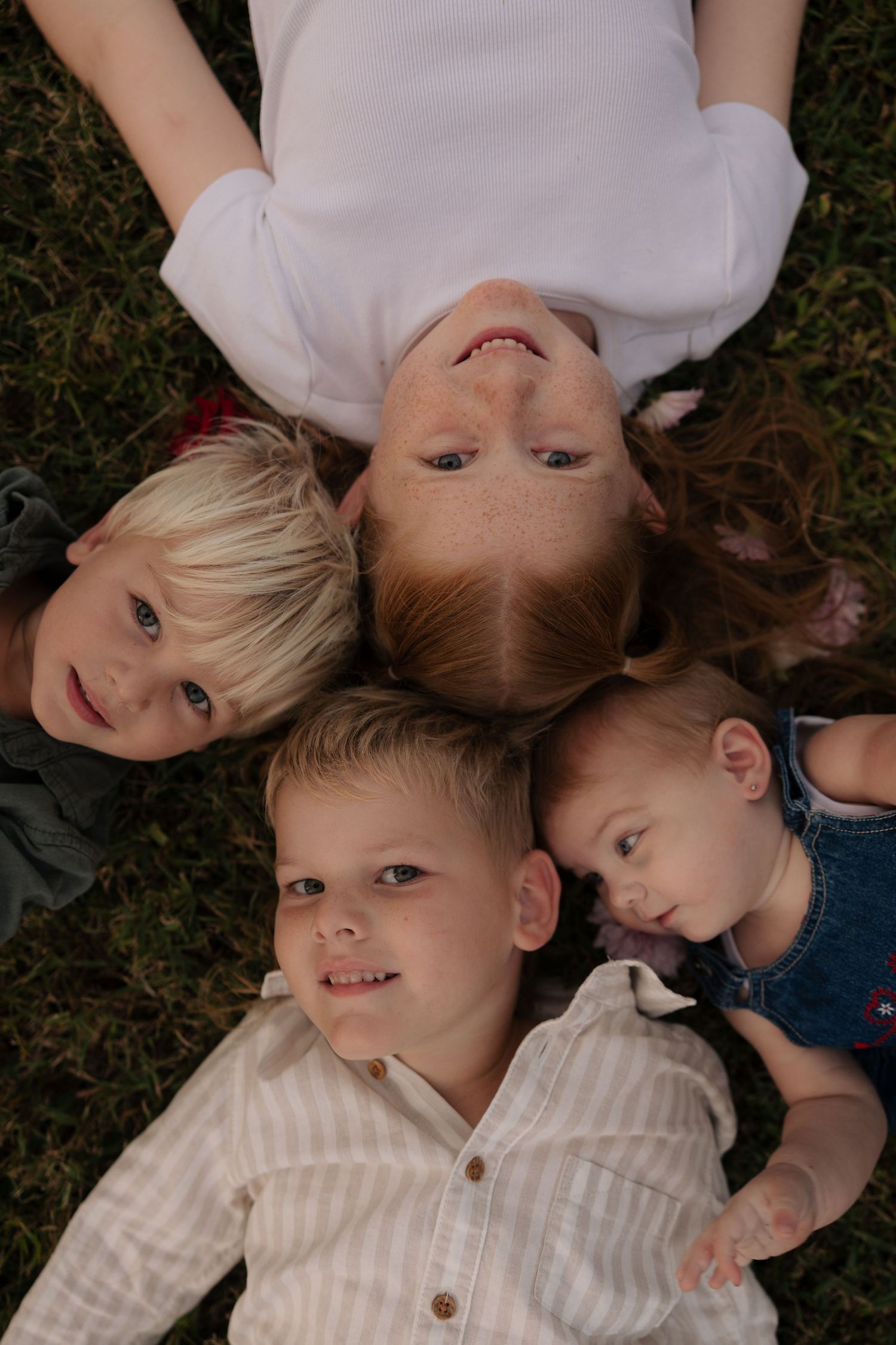Overhead view of children laying in a circle on grass with their heads together.