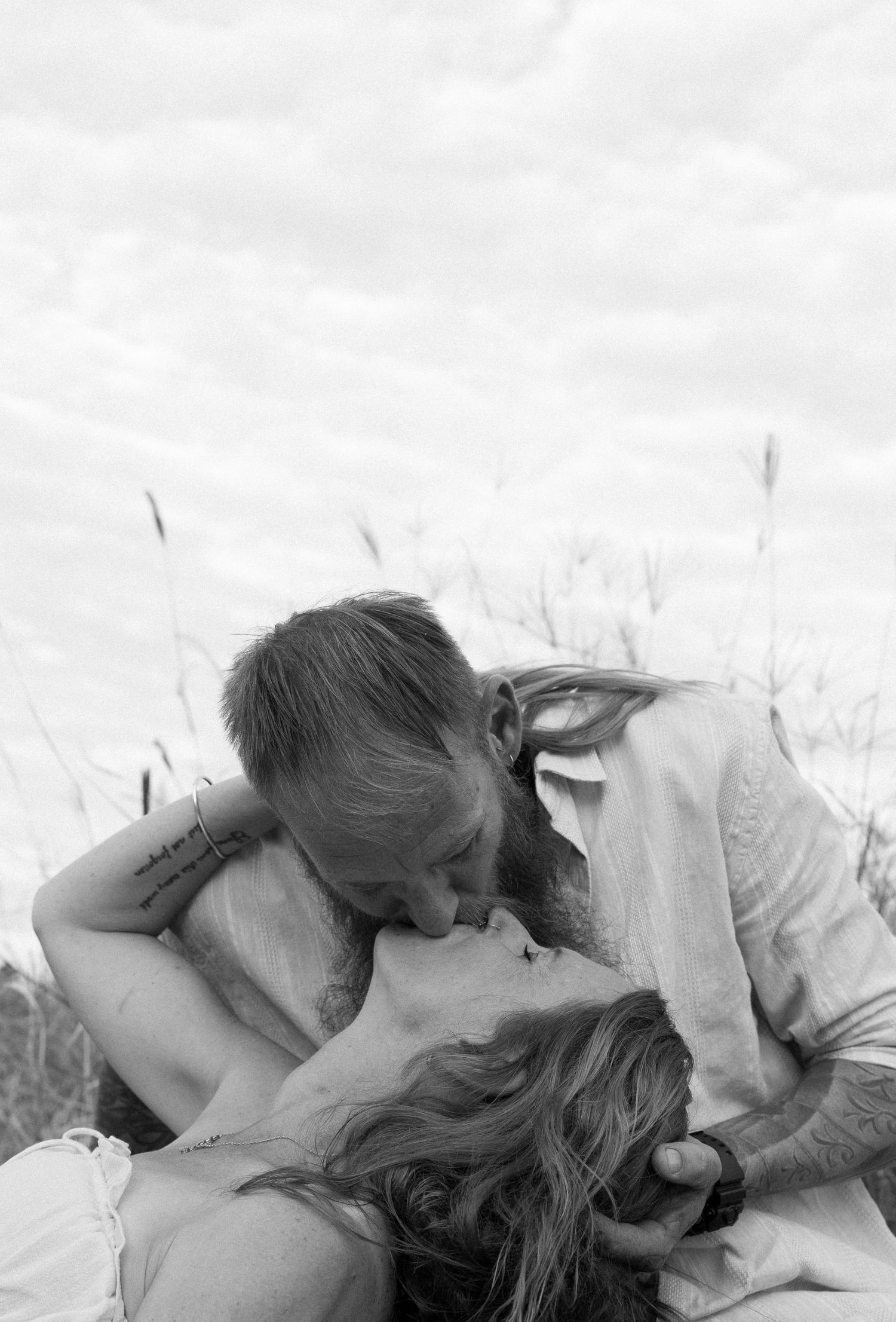 A romantic black and white photograph of a tender embrace and kiss in a grassy field.