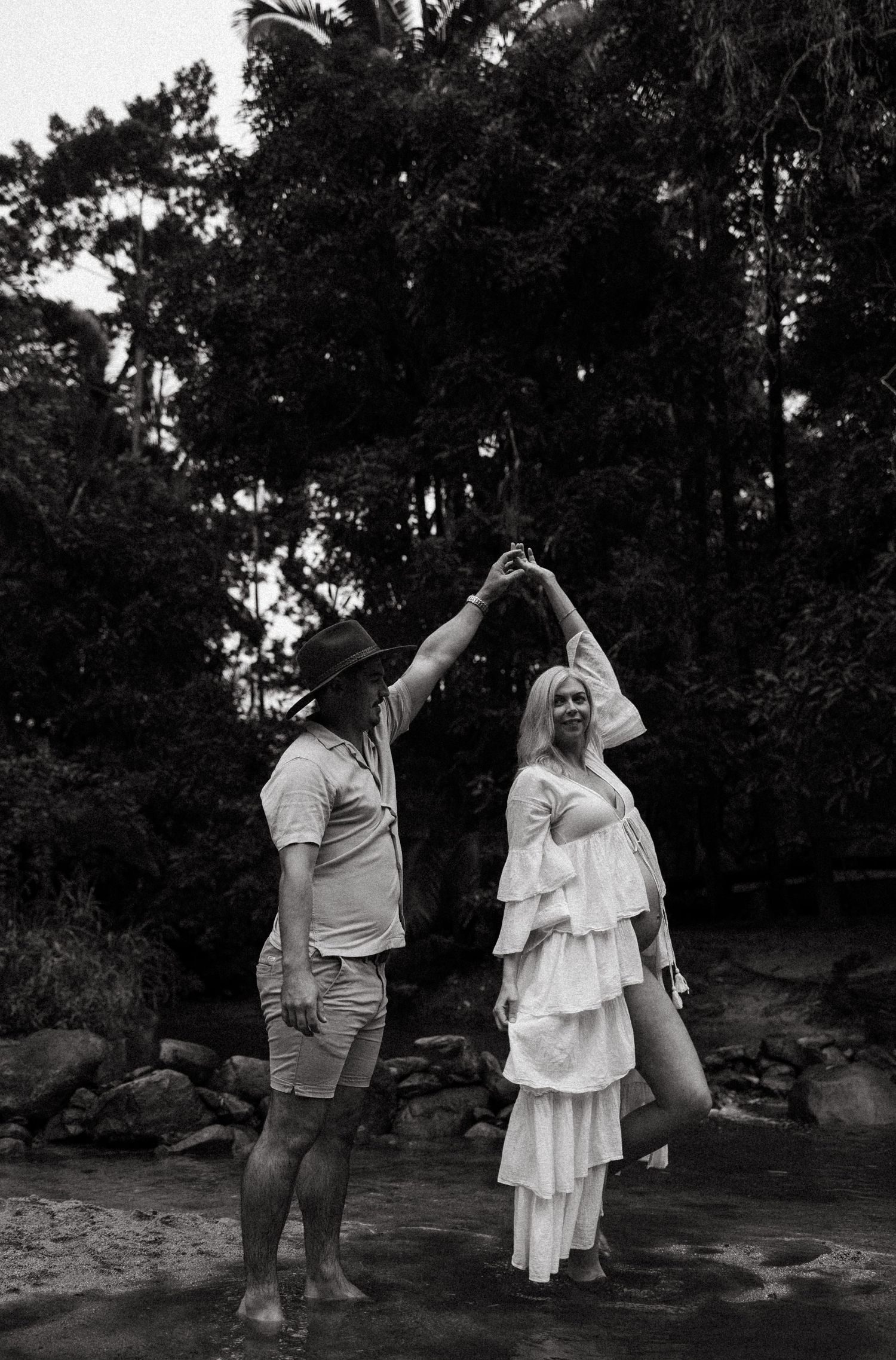 A couple dances together in a romantic black and white moment near a wooded area.