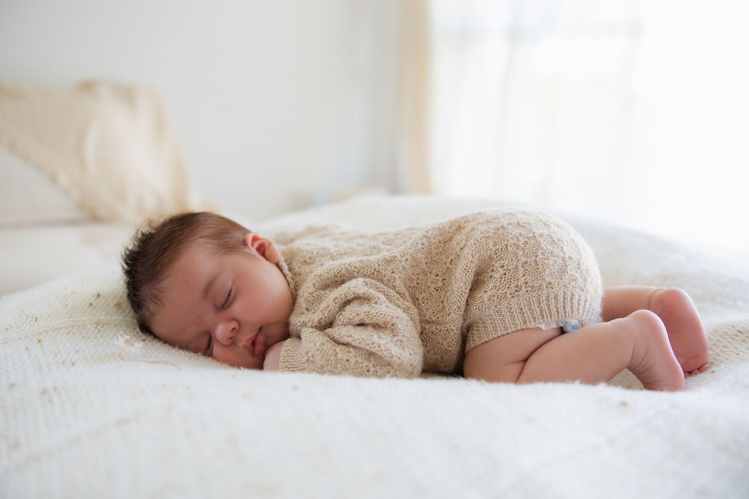 Peaceful naptime scene with sleeping infant in cozy sweater on white bedding.
