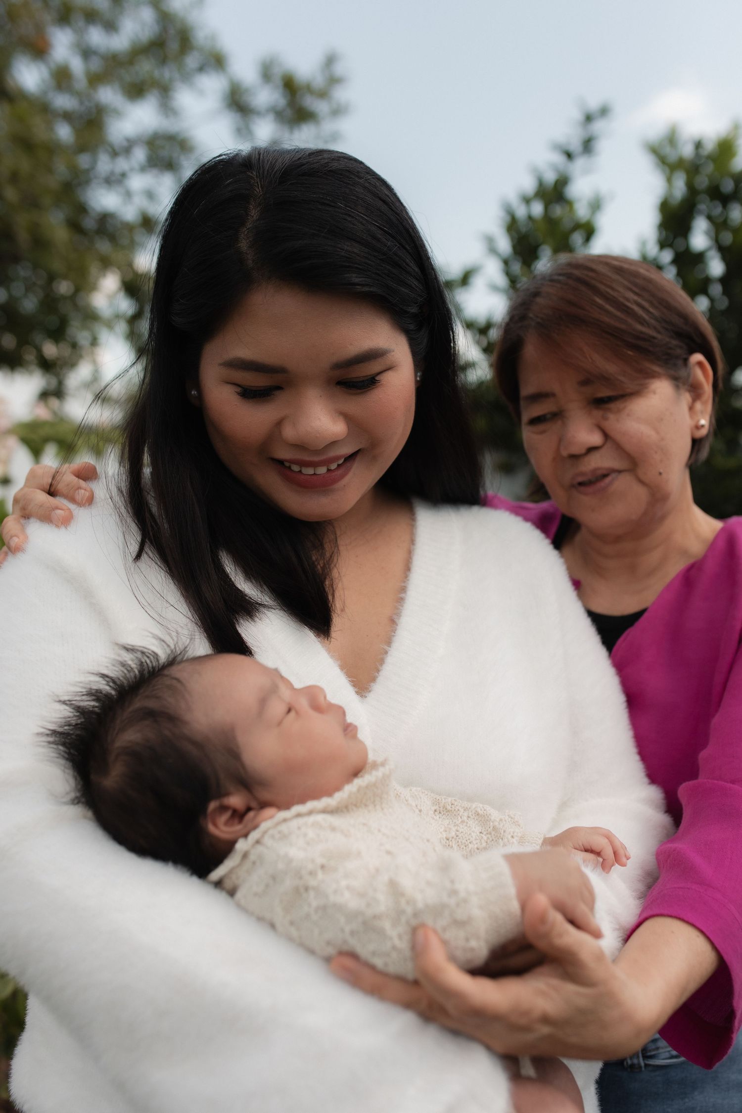 A touching outdoor portrait of three generations sharing a moment with a newborn baby.