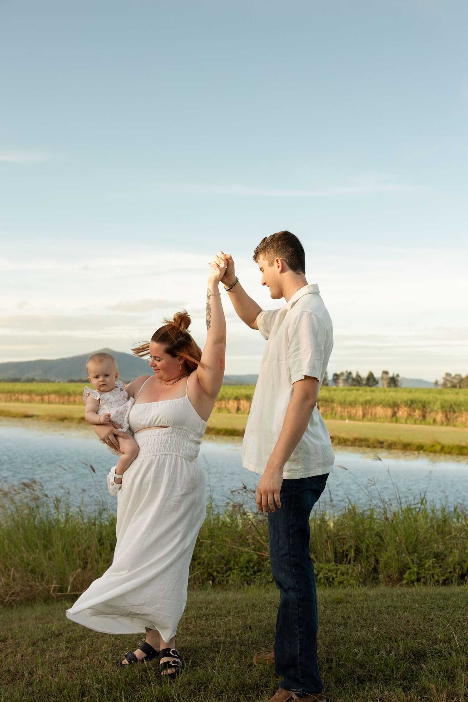 A family enjoying a playful moment together by a lake during golden hour with mountains in the background.