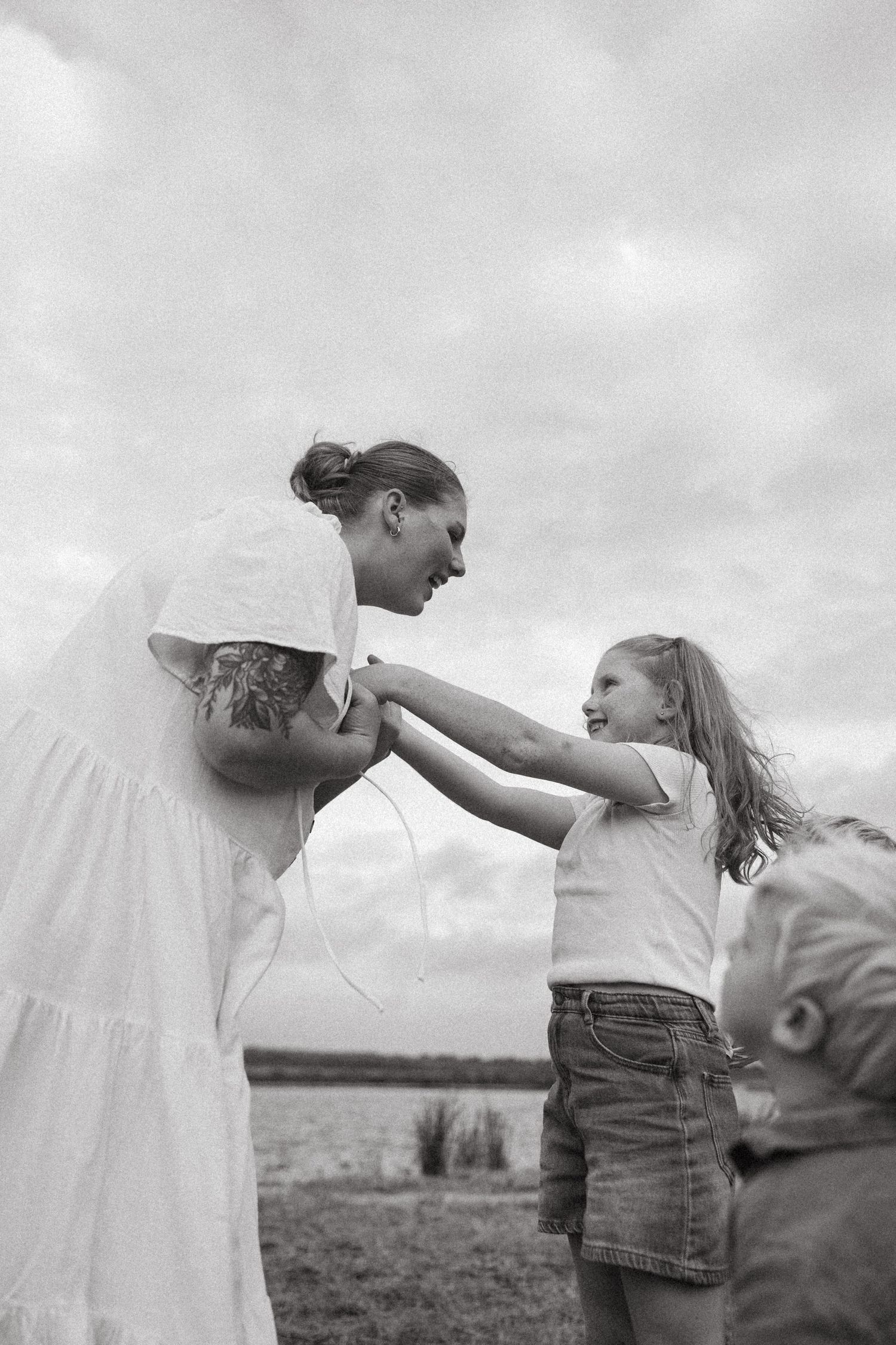 A black and white candid photo of people interacting outdoors against a cloudy sky.