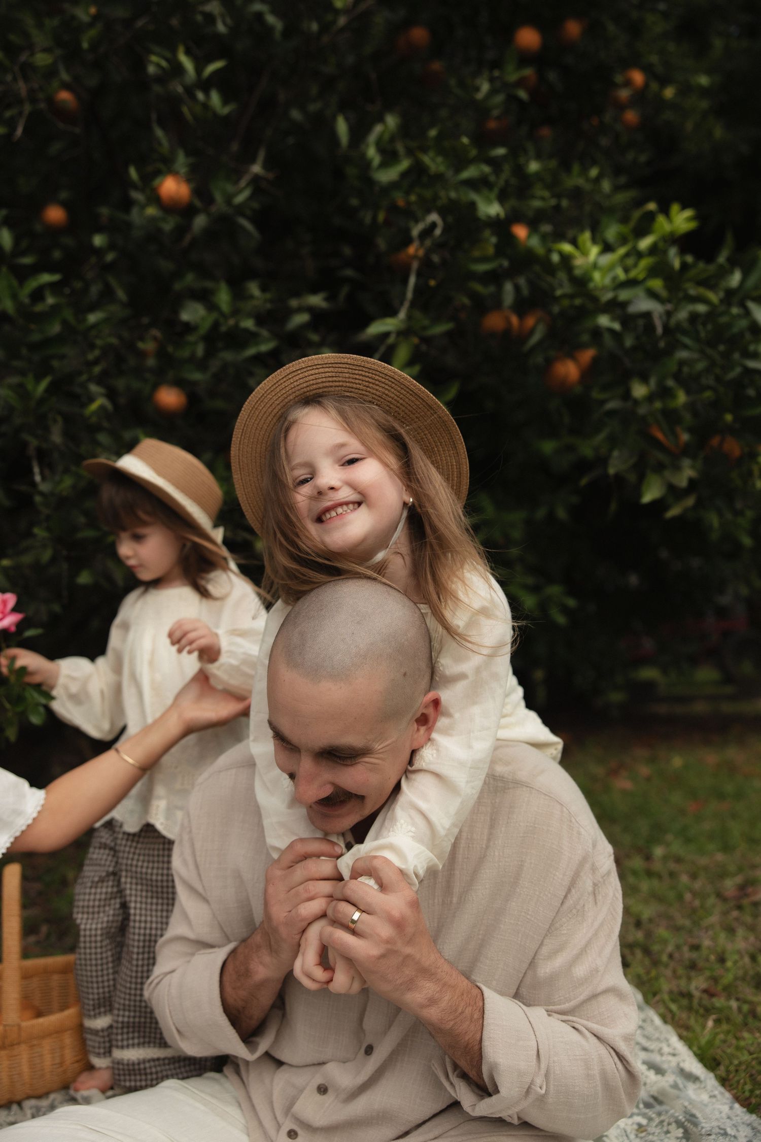 Sweet candid moments captured outdoors in front of orange trees showing playful laughter in neutral toned clothing.