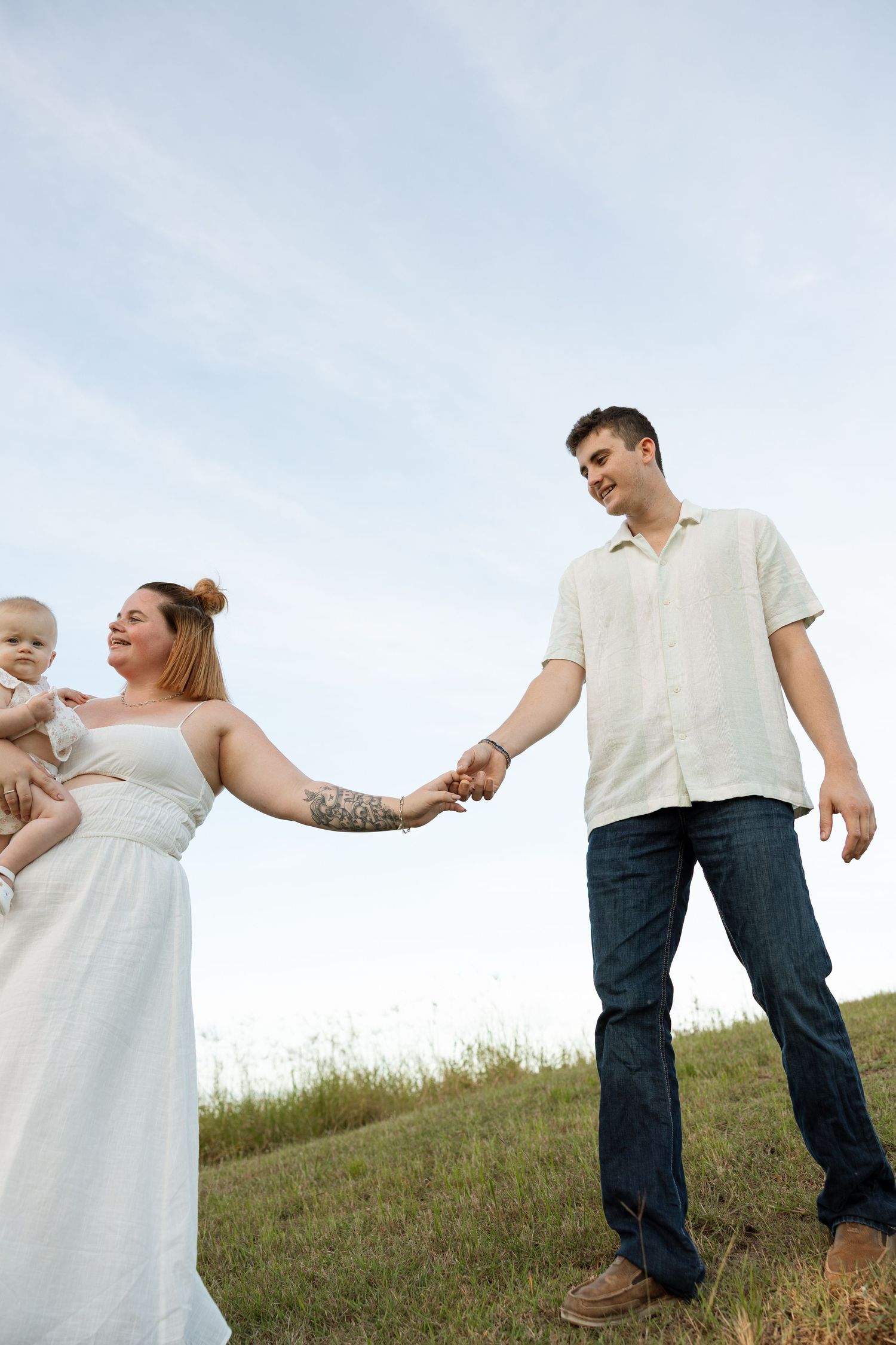 A family holding hands while standing on a grassy hill against a blue sky.
