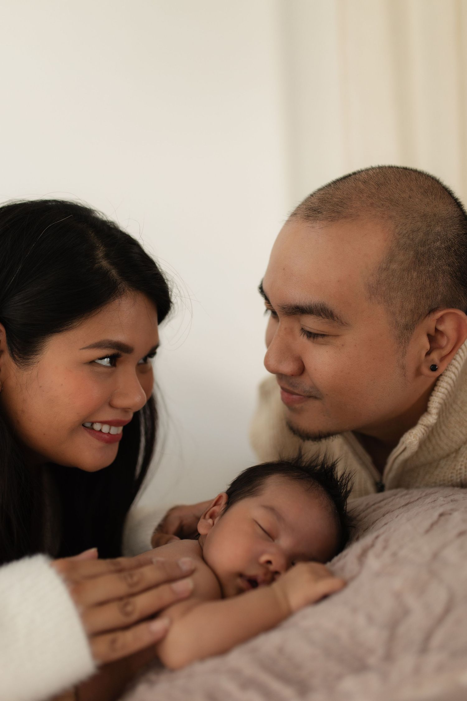 An intimate family moment with a sleeping baby nestled between parents in a cozy indoor setting.