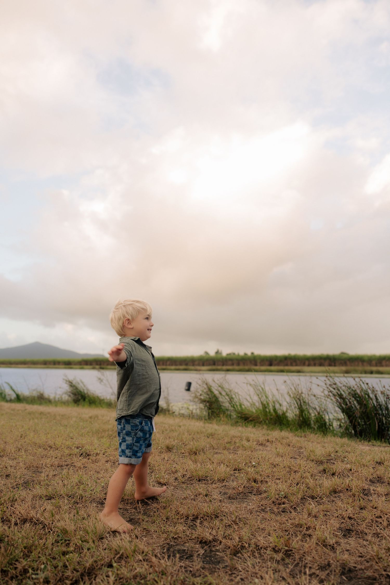 Small child standing barefoot on grassy hill overlooking lake landscape.
