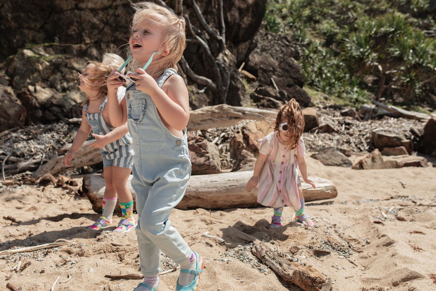 Group of children playing and dancing on a rocky beach with driftwood.