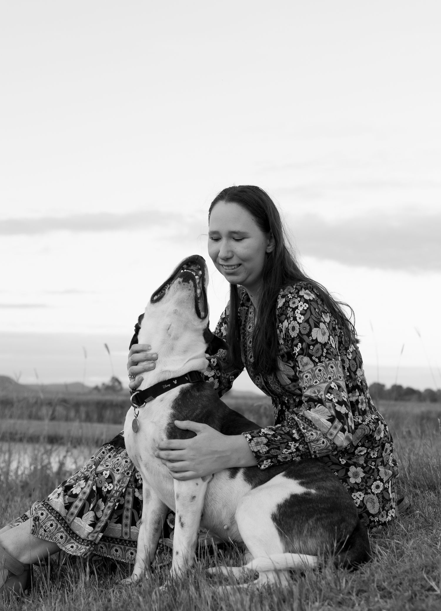 Grayscale portrait of a dog and owner sharing an intimate moment together in a field at sunset.