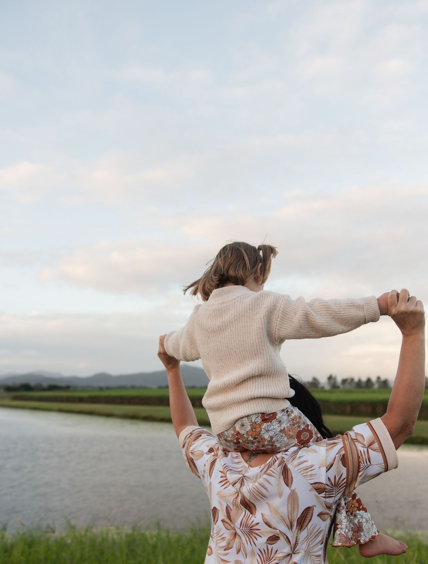 Sunset playtime by the water with coordinated floral outfits in a rural landscape.