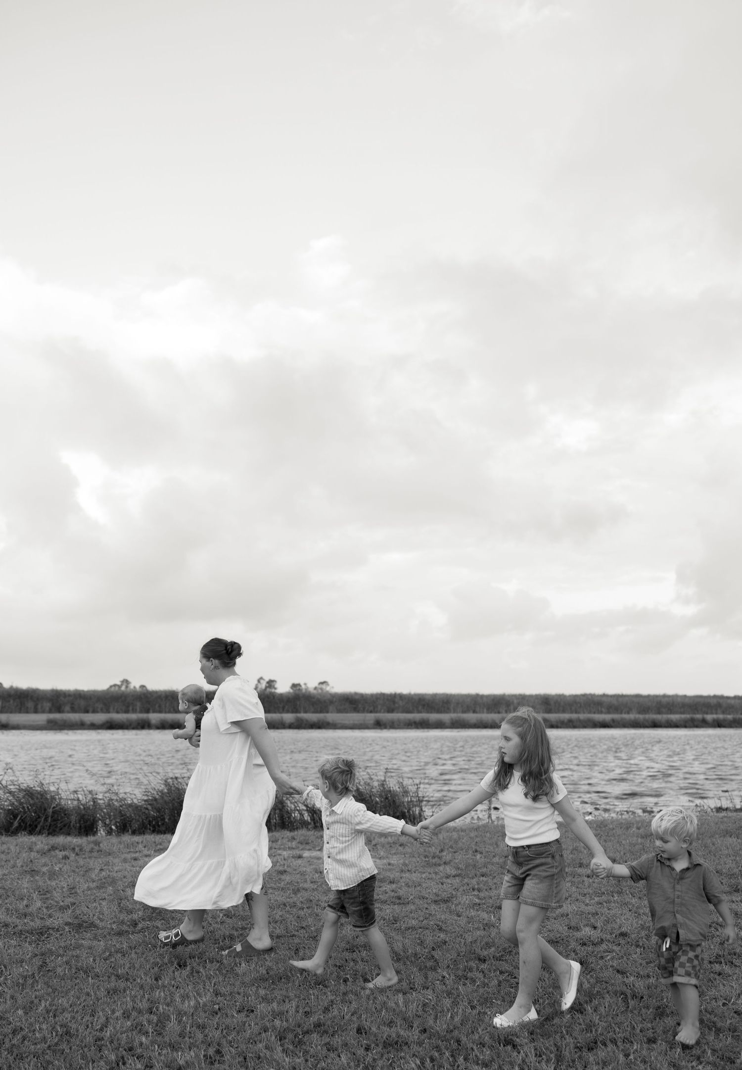 A line of people holding hands walking together by the water in black and white.