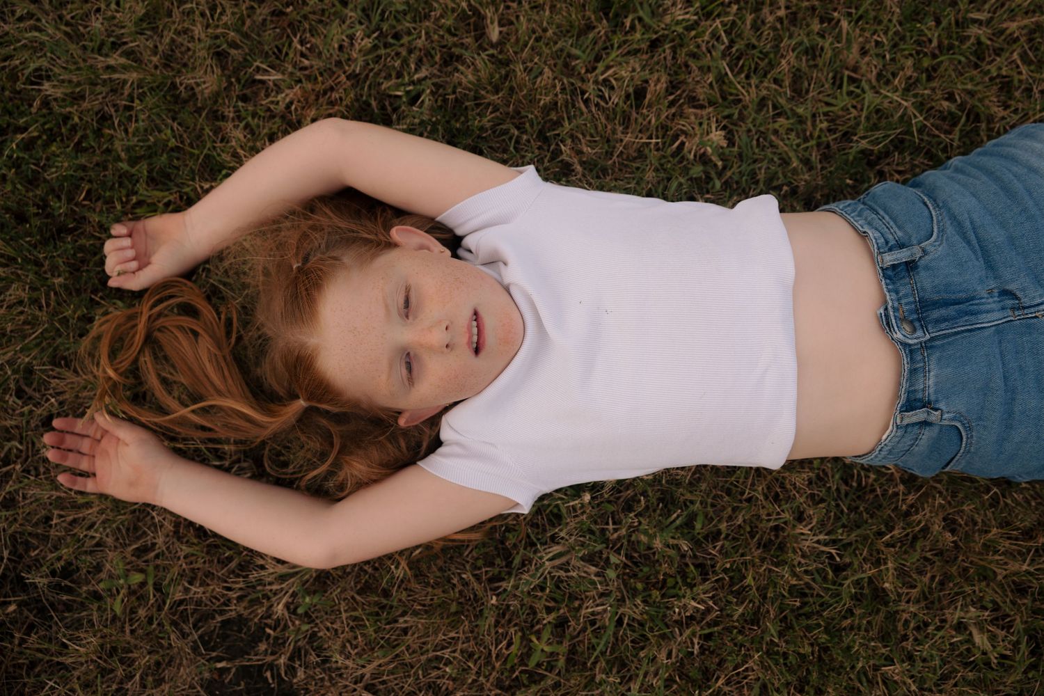 Child lying peacefully on grass wearing casual summer attire.