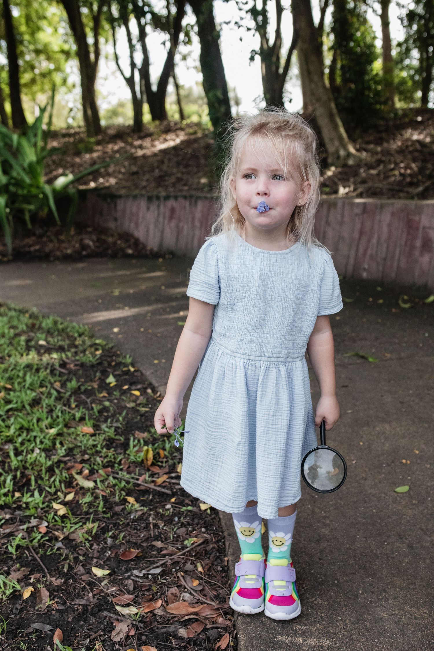 Child in blue dress with colorful stained face standing on garden path wearing rainbow socks.