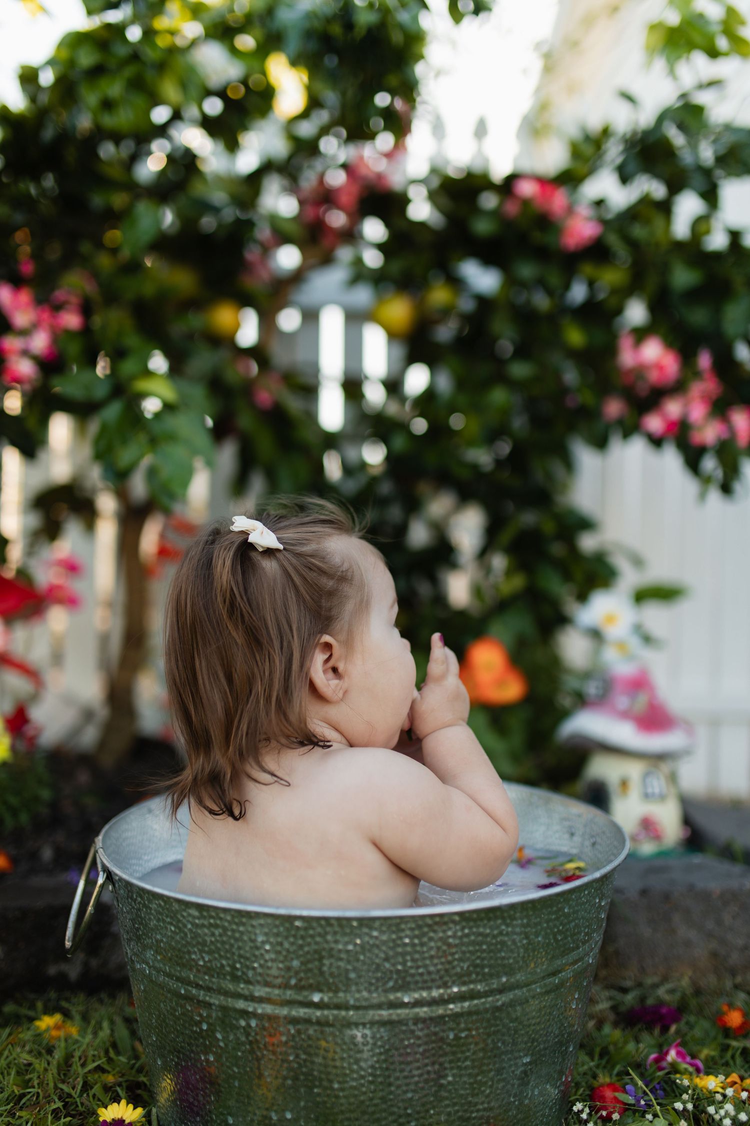 Child taking bath in vintage metal tub surrounded by blooming garden flowers.