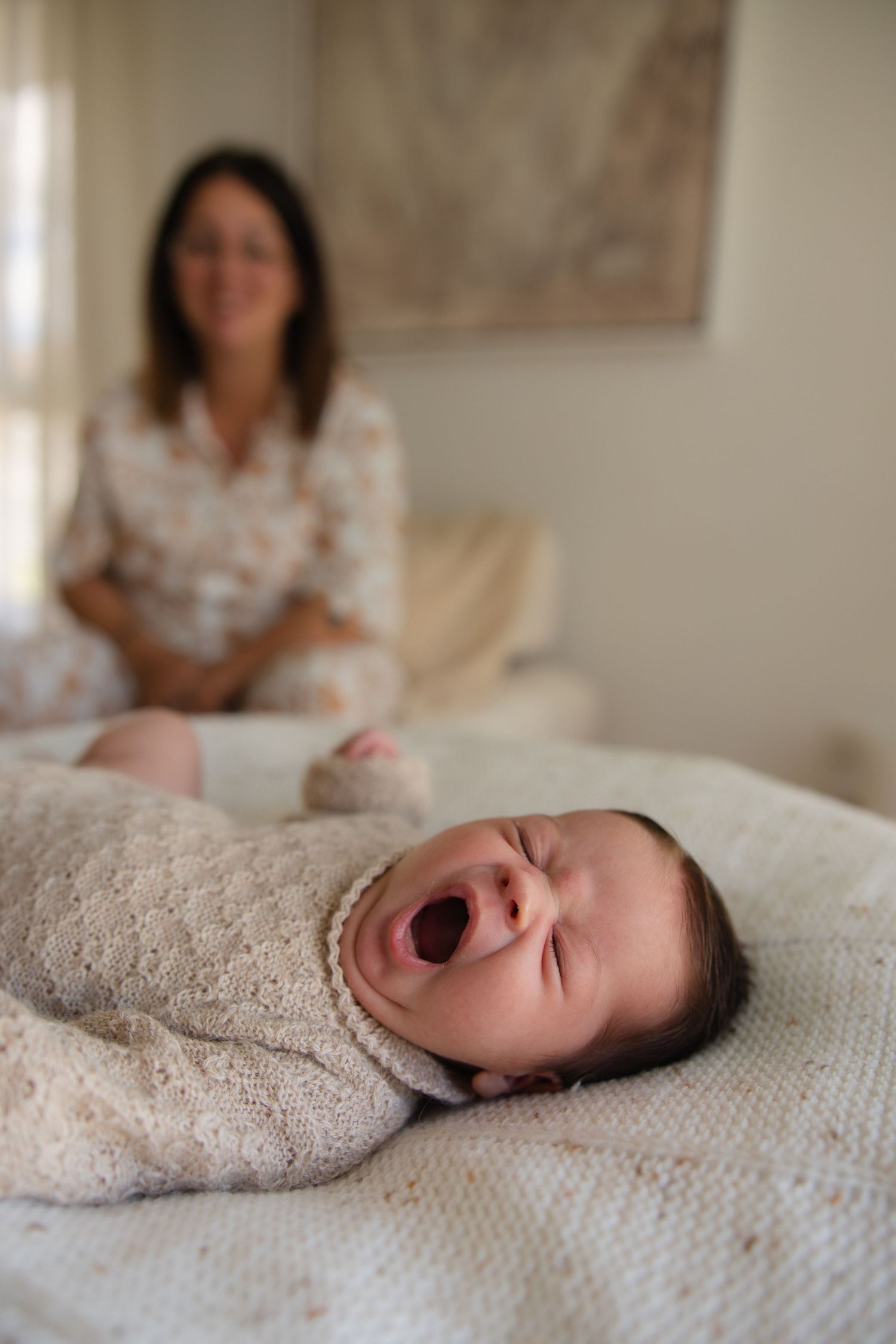 Sleeping baby in cream sweater yawning on white bedding.