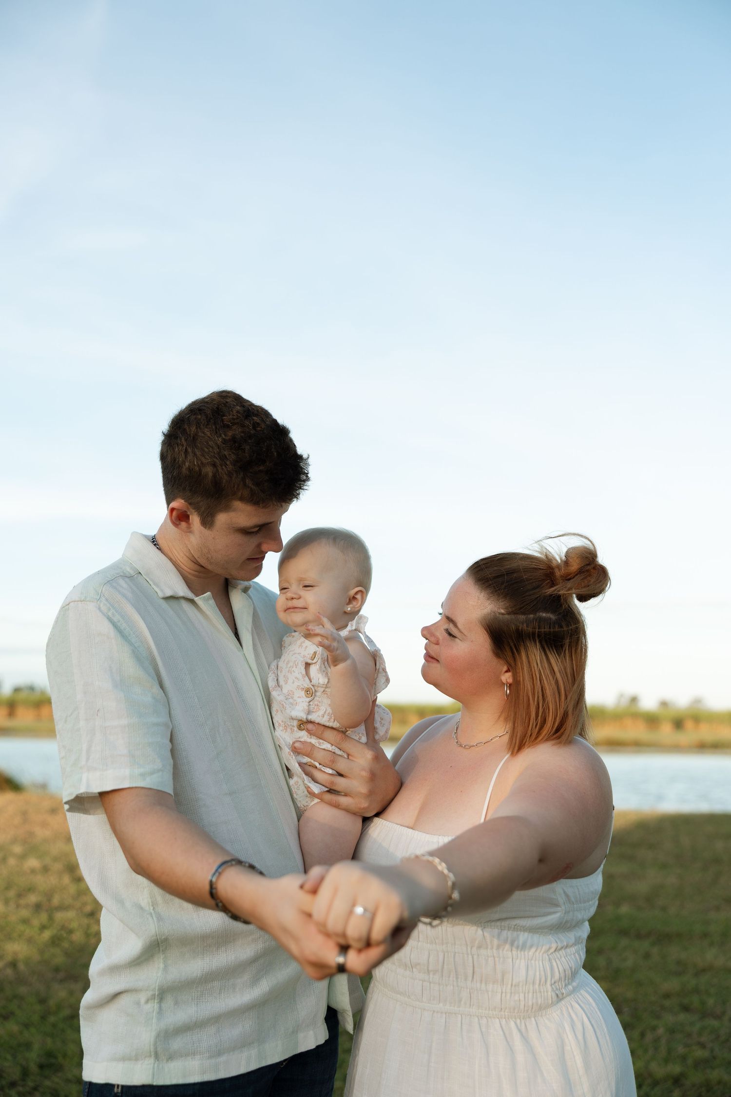 A tender family moment outdoors with a baby against a lakeside backdrop at sunset.