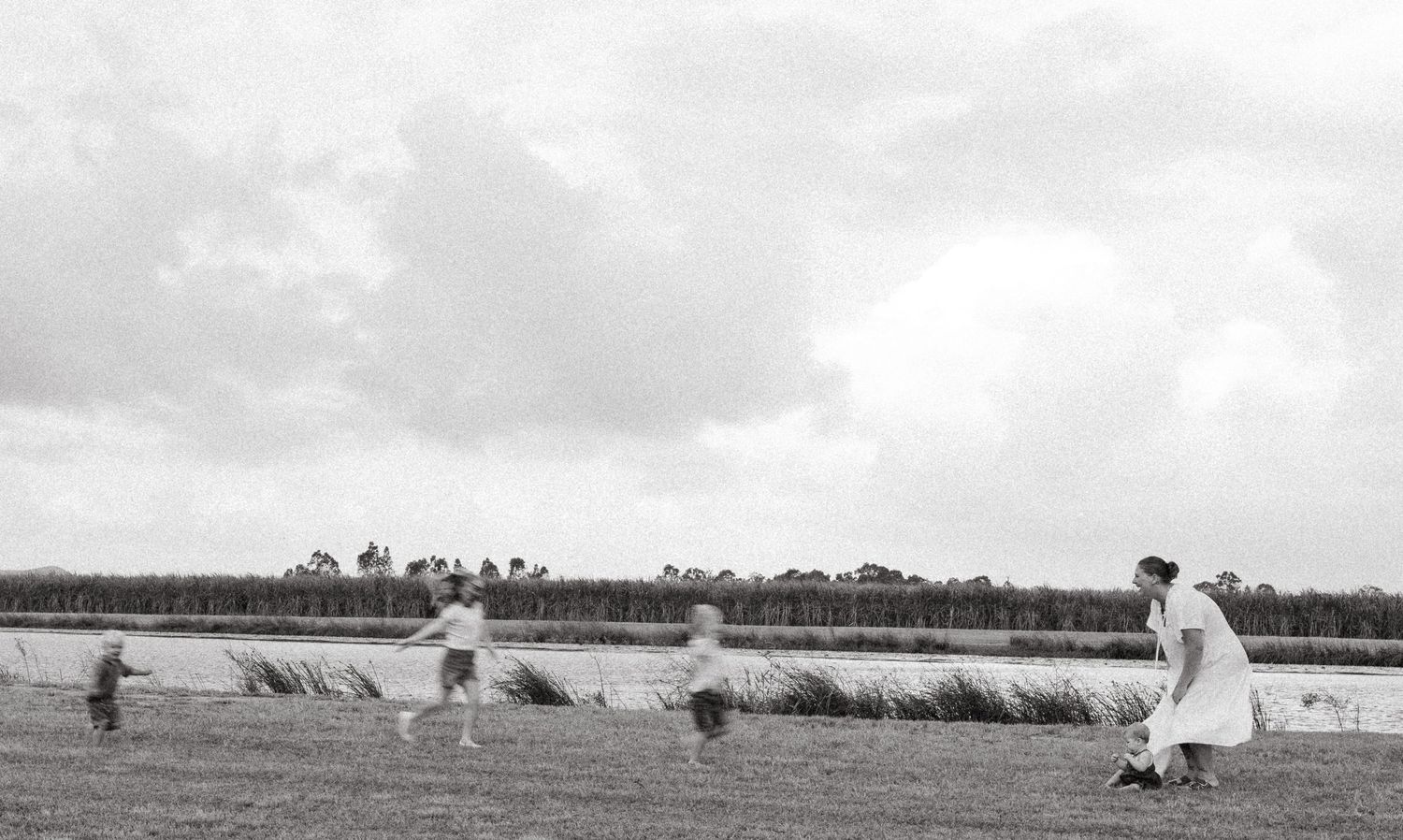 People enjoying a playful moment in a field by the water, captured in black and white.