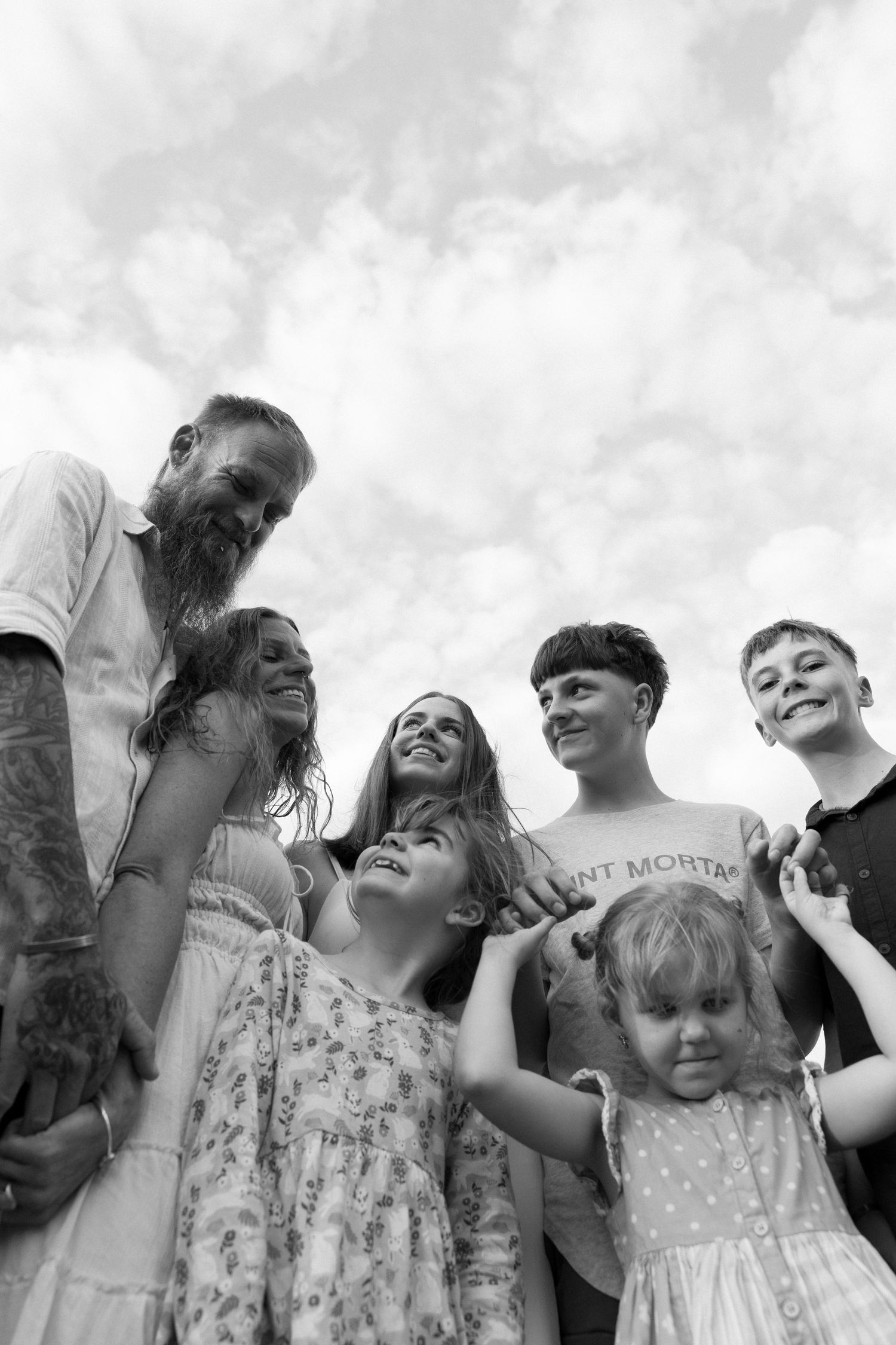 A black and white low-angle shot of a family group smiling together against a cloudy sky.