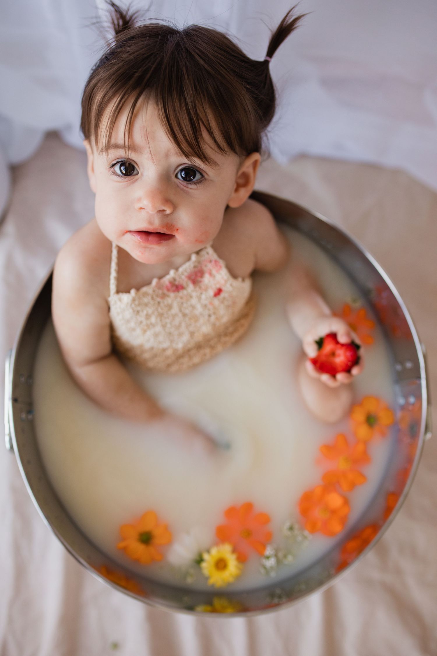 Small child enjoying a milk bath with colorful floating flowers and a slice of bread.