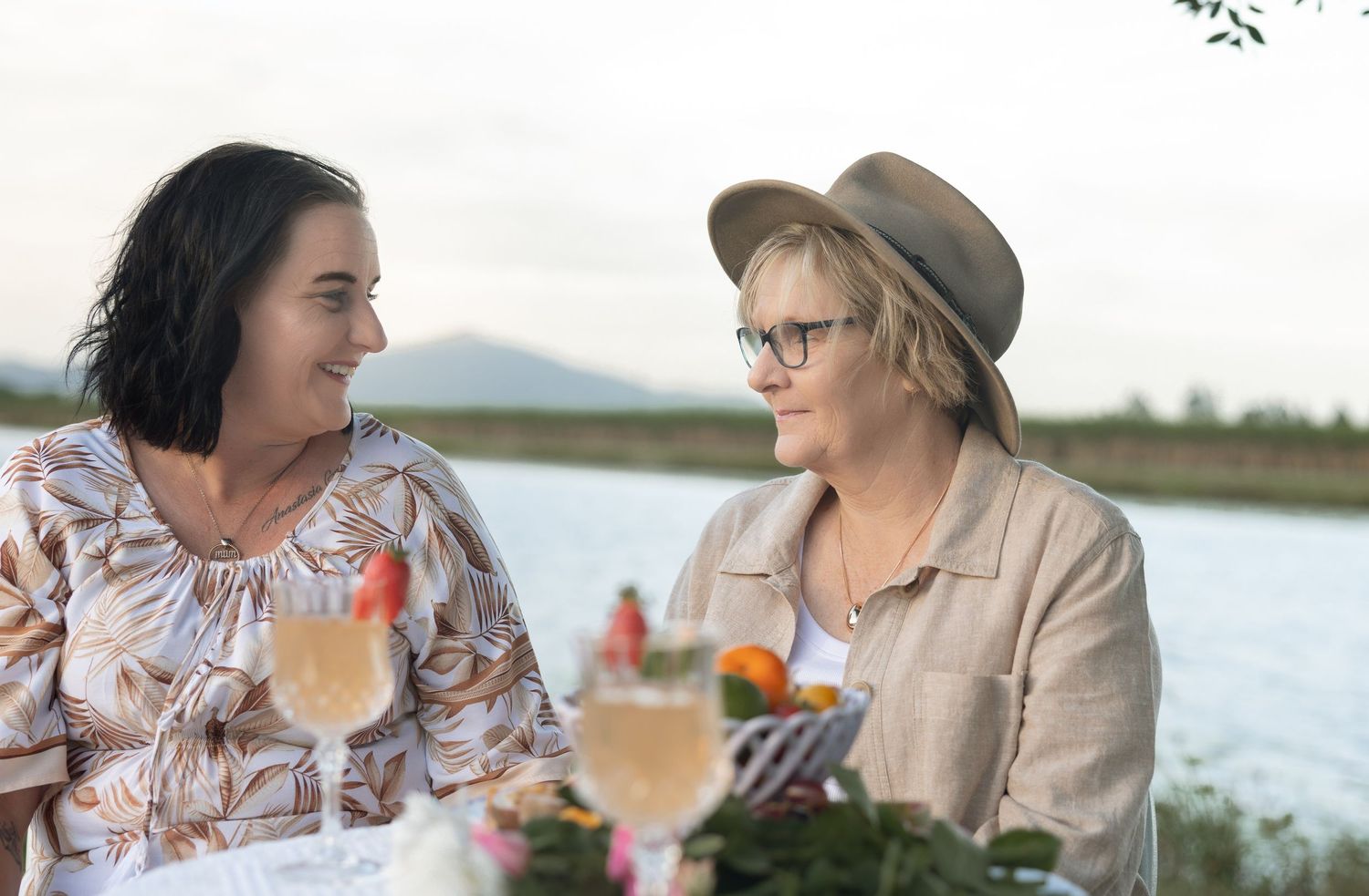Friends enjoying drinks and conversation by a scenic lake during golden hour.