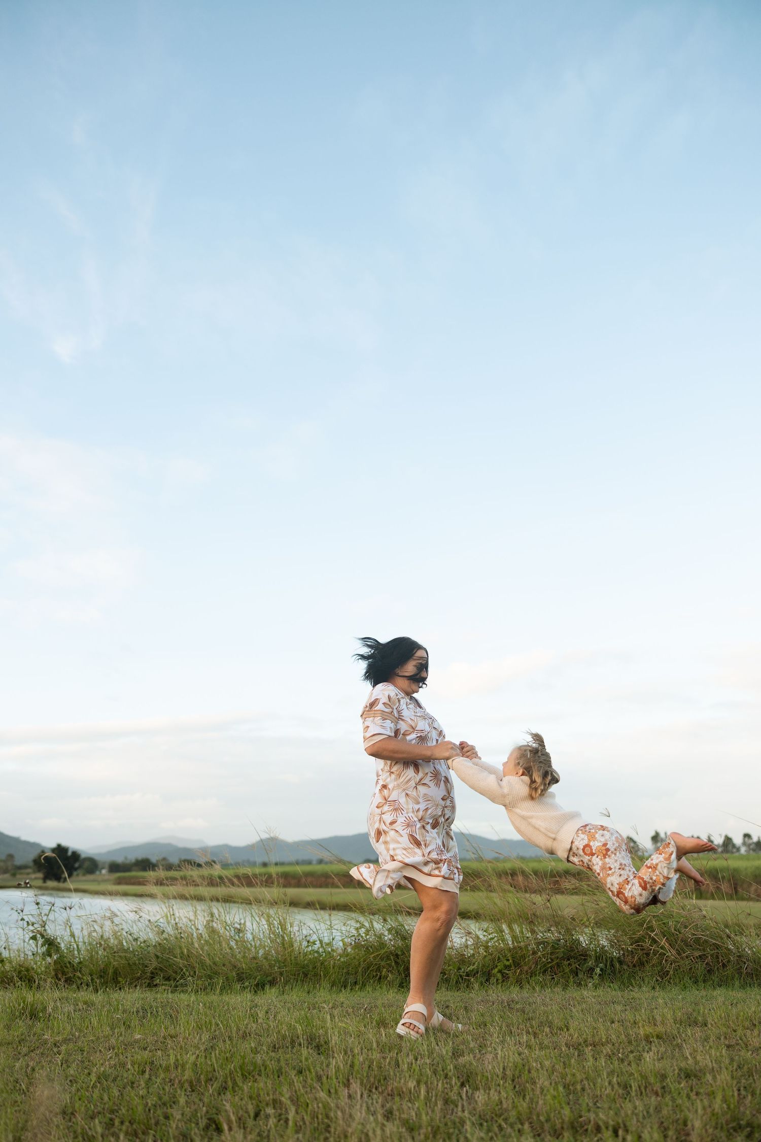 Carefree spinning moment captured against a serene waterfront setting in matching floral outfits.