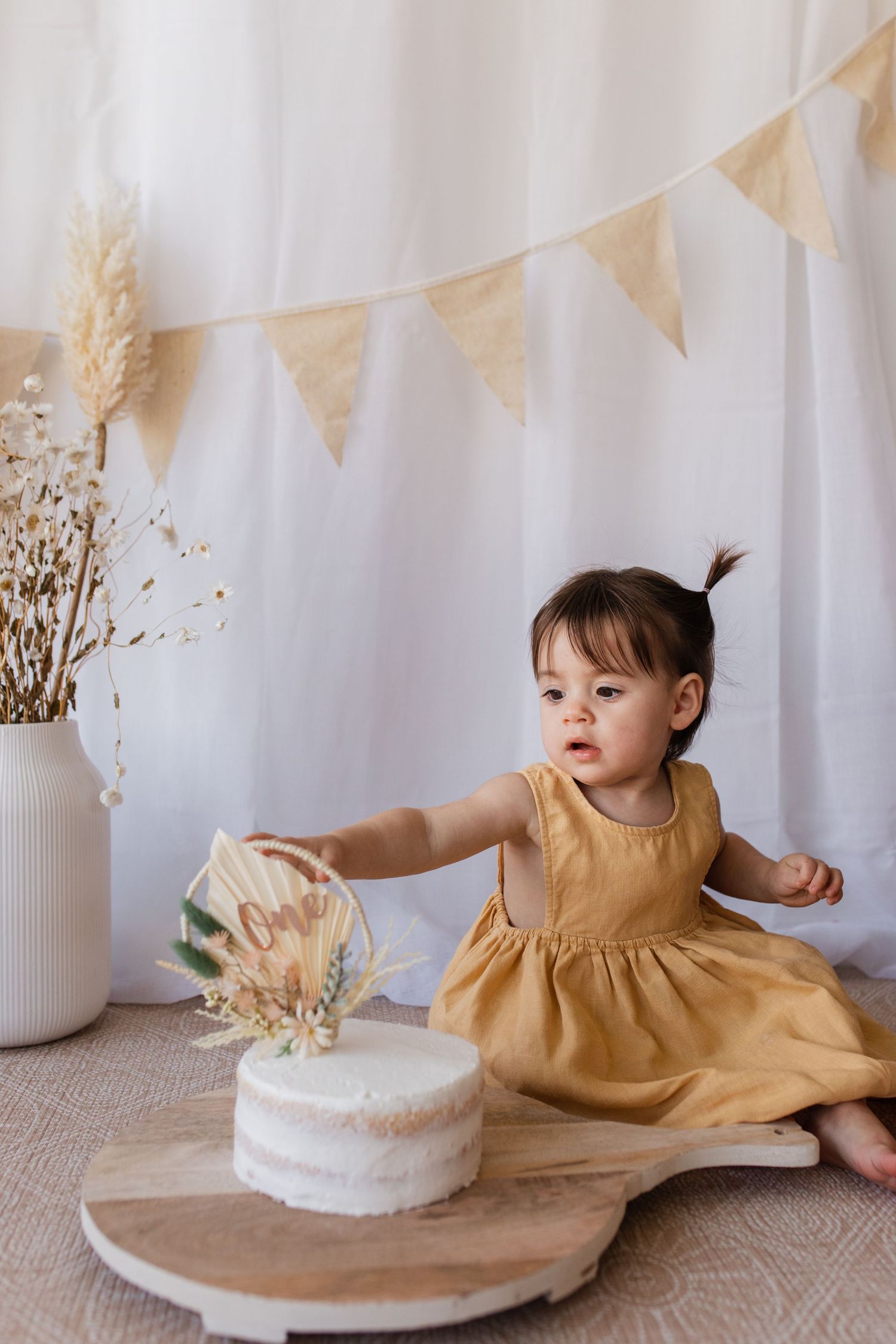 Birthday cake decorating scene with bunting and dried flowers in background.