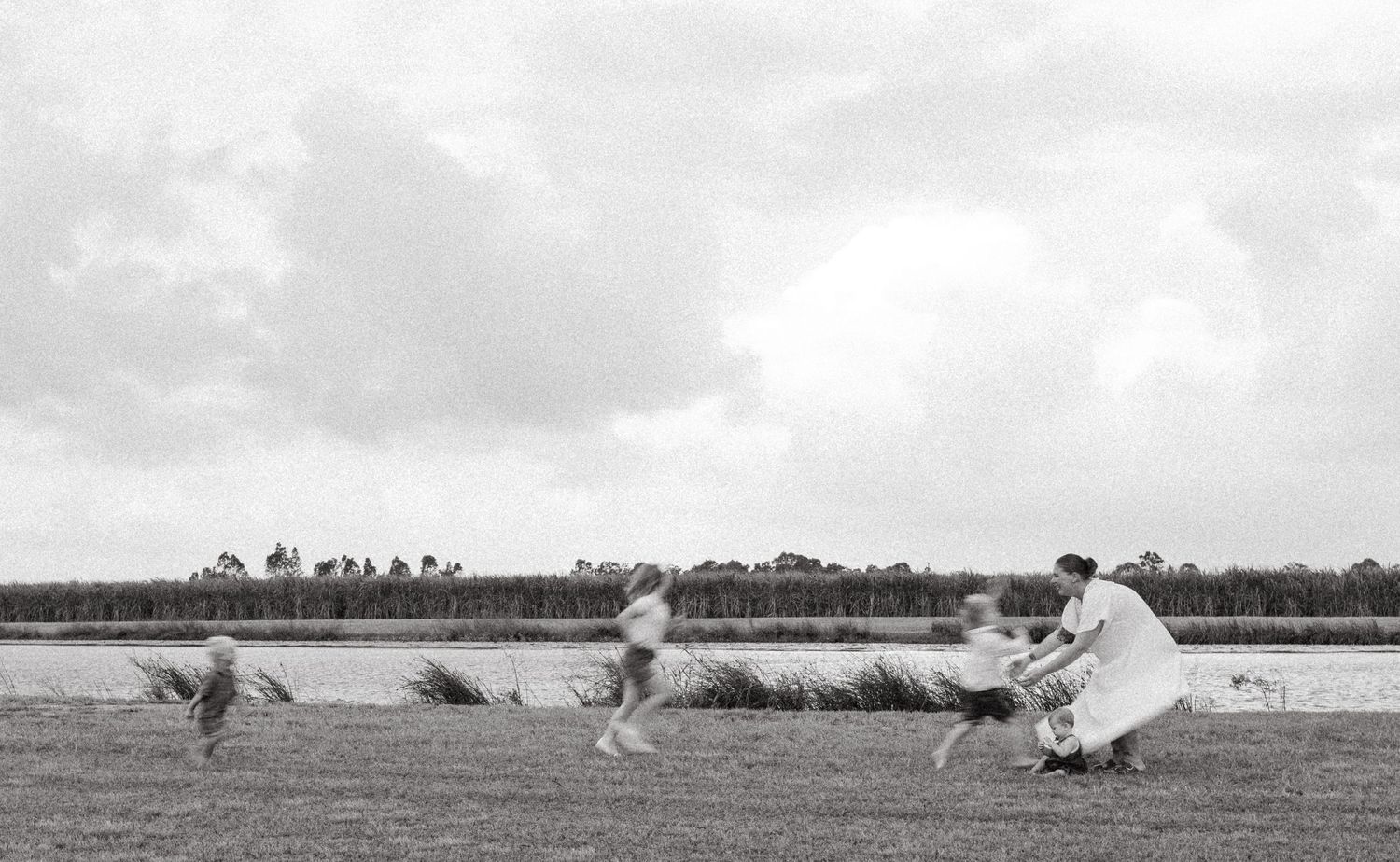 A black and white scene of family members playing by a lake with flowing dress fabric.