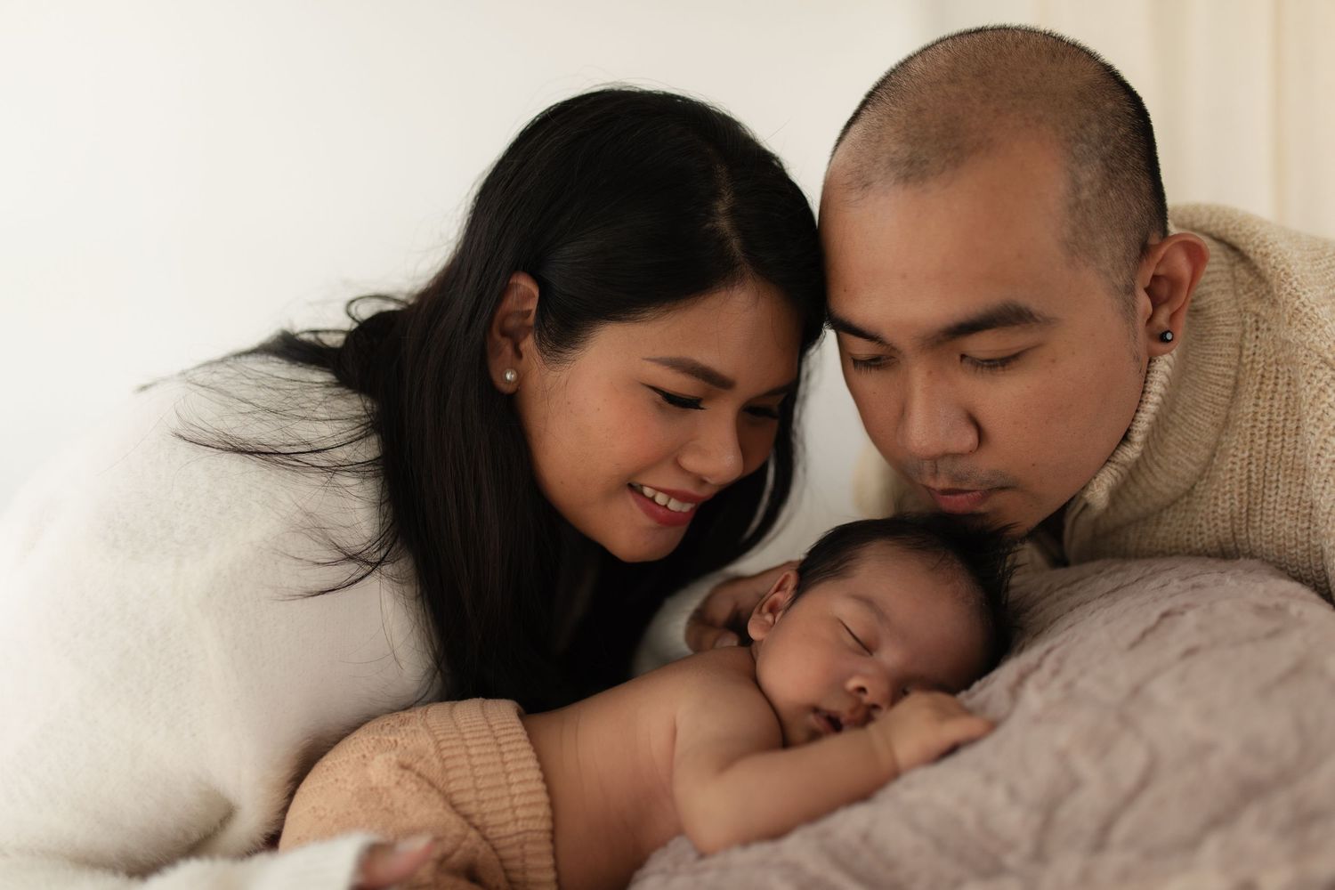 A warm indoor family portrait showing tender moments with their sleeping newborn.